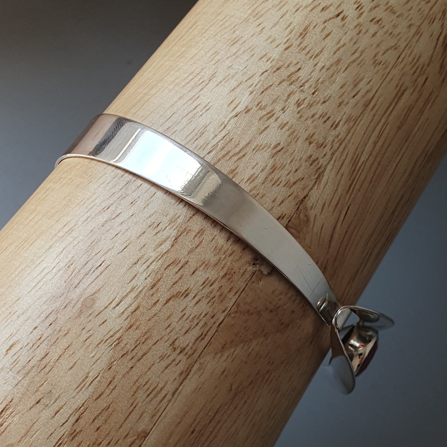 Silver bracelet or bangle wrapped around a wooden surface.