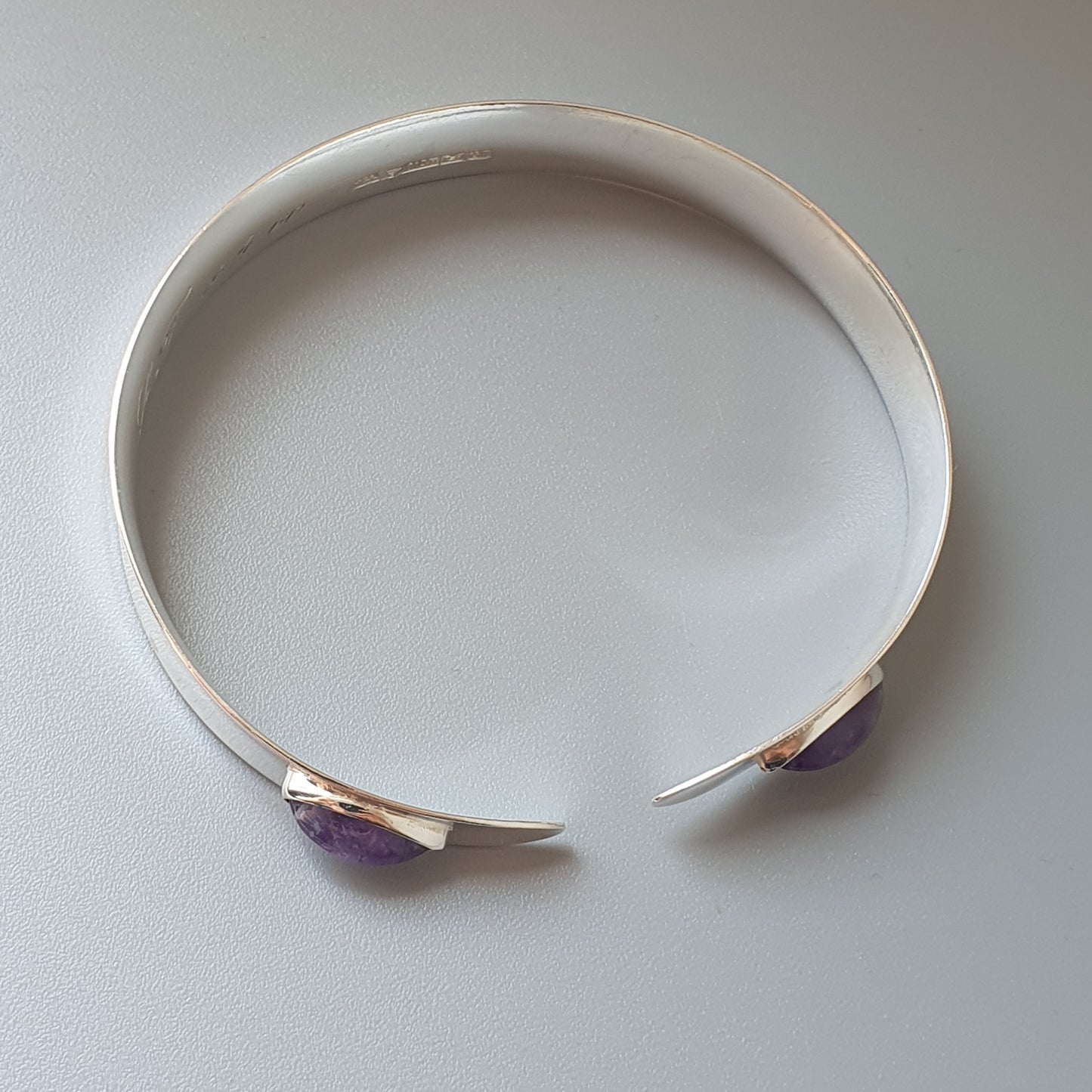 Silver cuff bracelet with purple gemstone accents at the open ends.