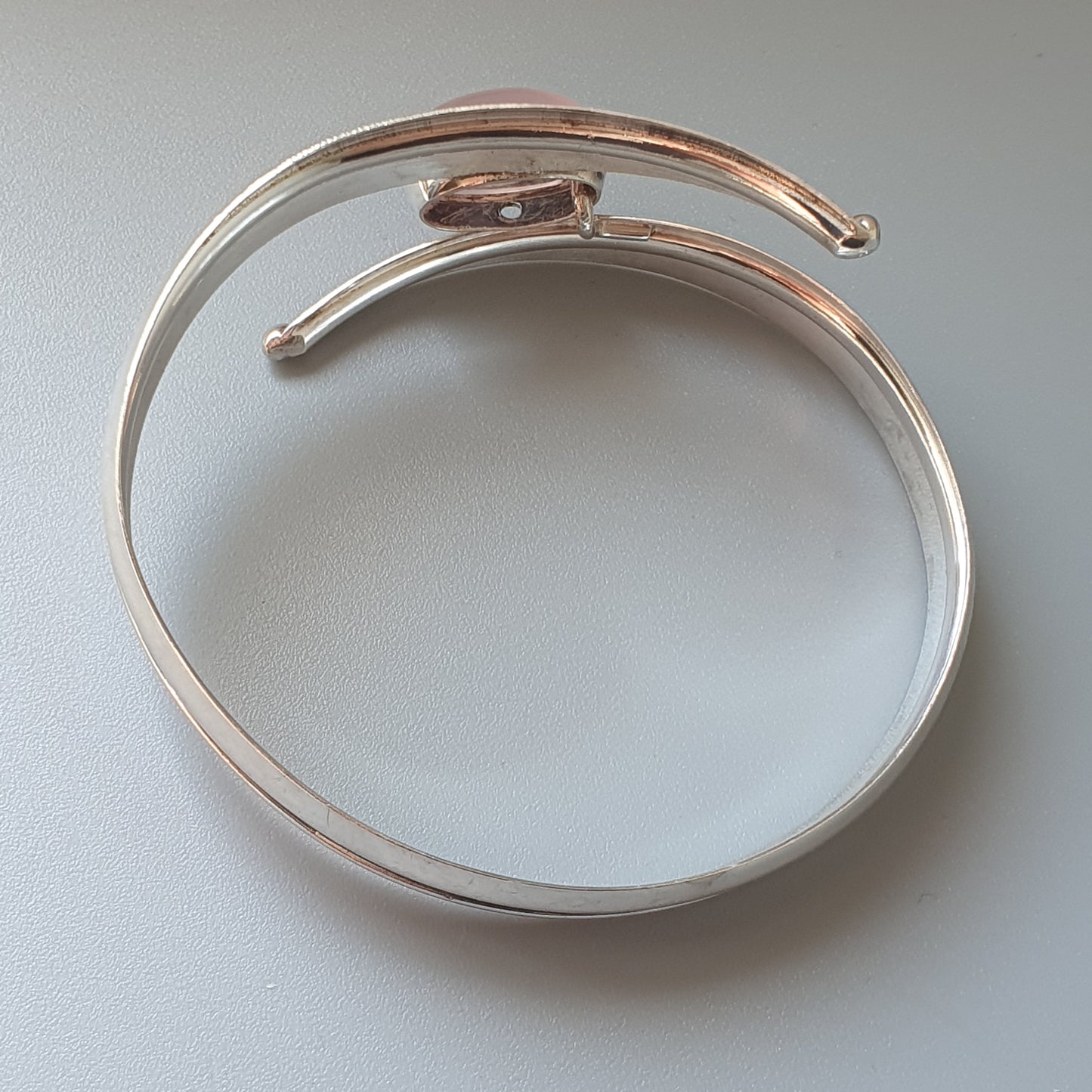 Curved metallic bracelet with overlapping ends in silver and rose gold tones.