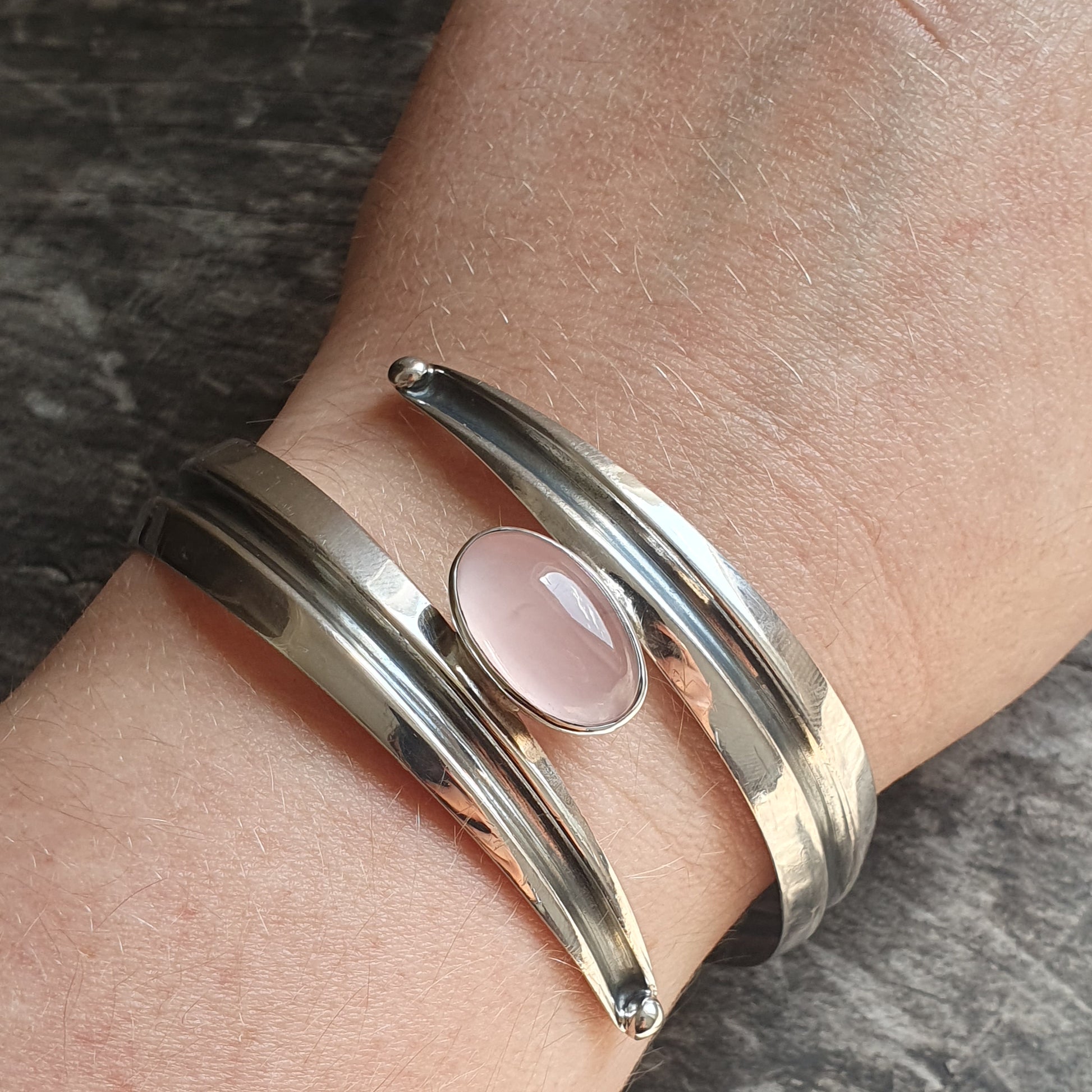 Silver cuff bracelet with a pink gemstone or cabochon centerpiece.