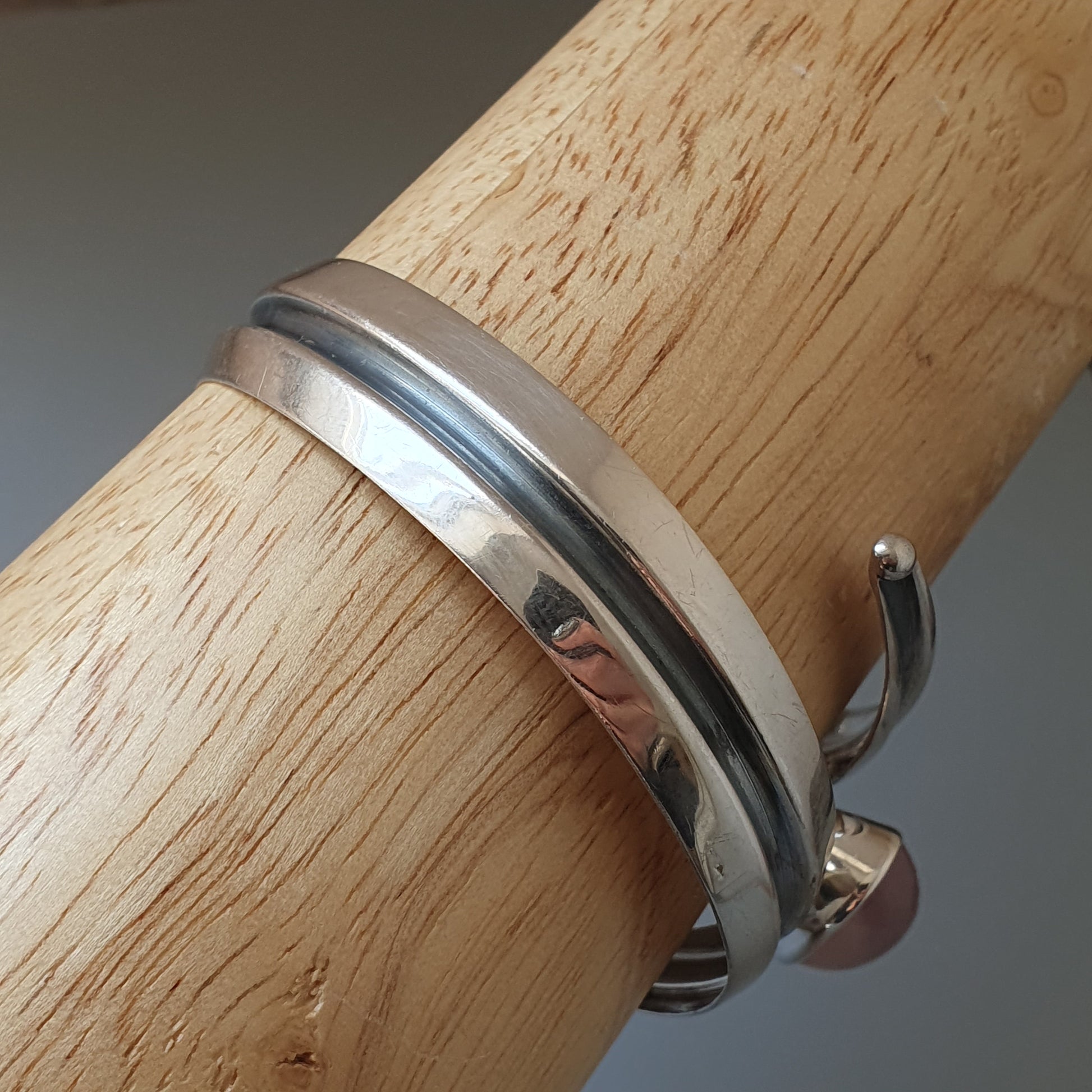 Silver metal bracelet or bangle wrapped around a wooden cylinder.