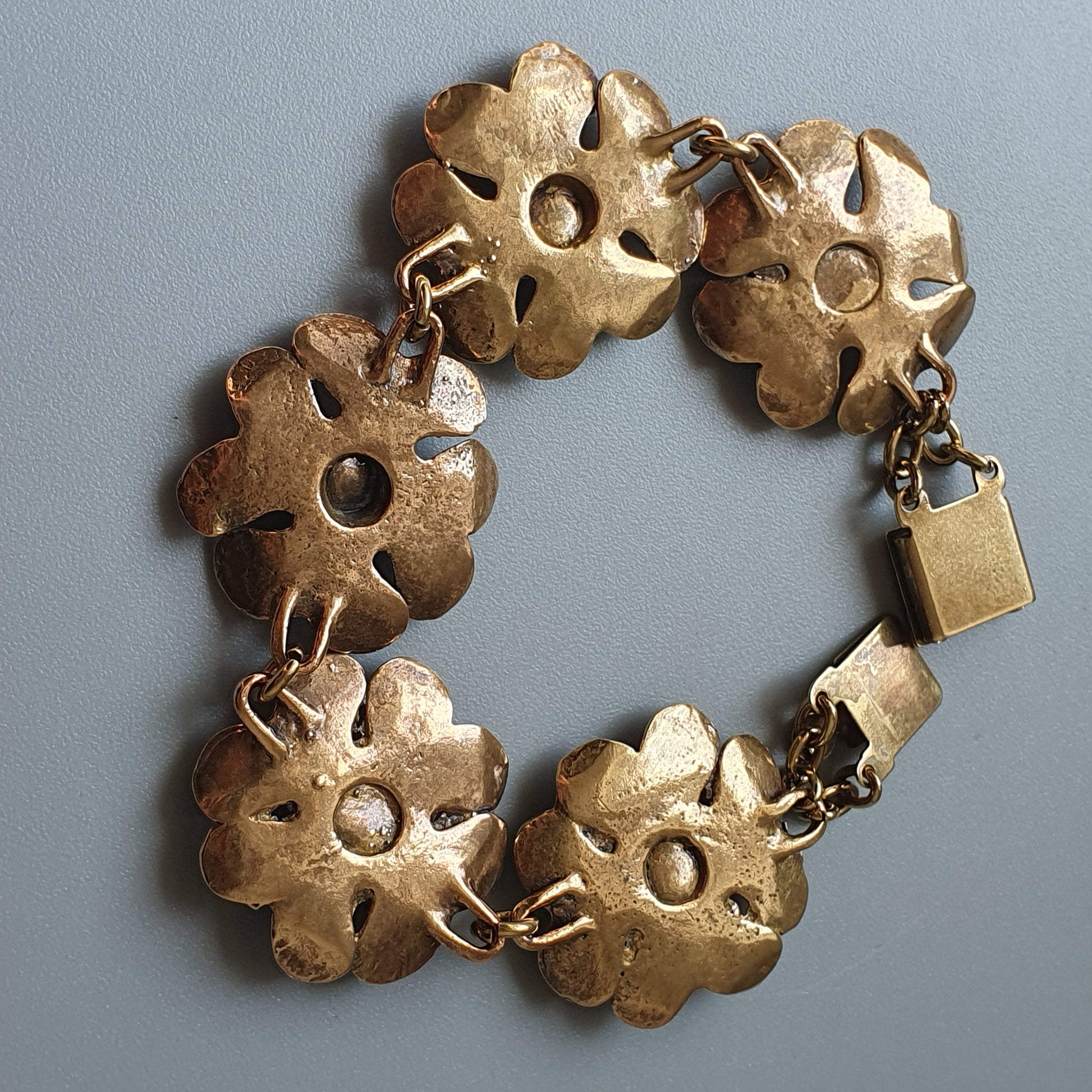 Gold-toned flower-shaped bracelet with five linked floral elements and a small padlock clasp.