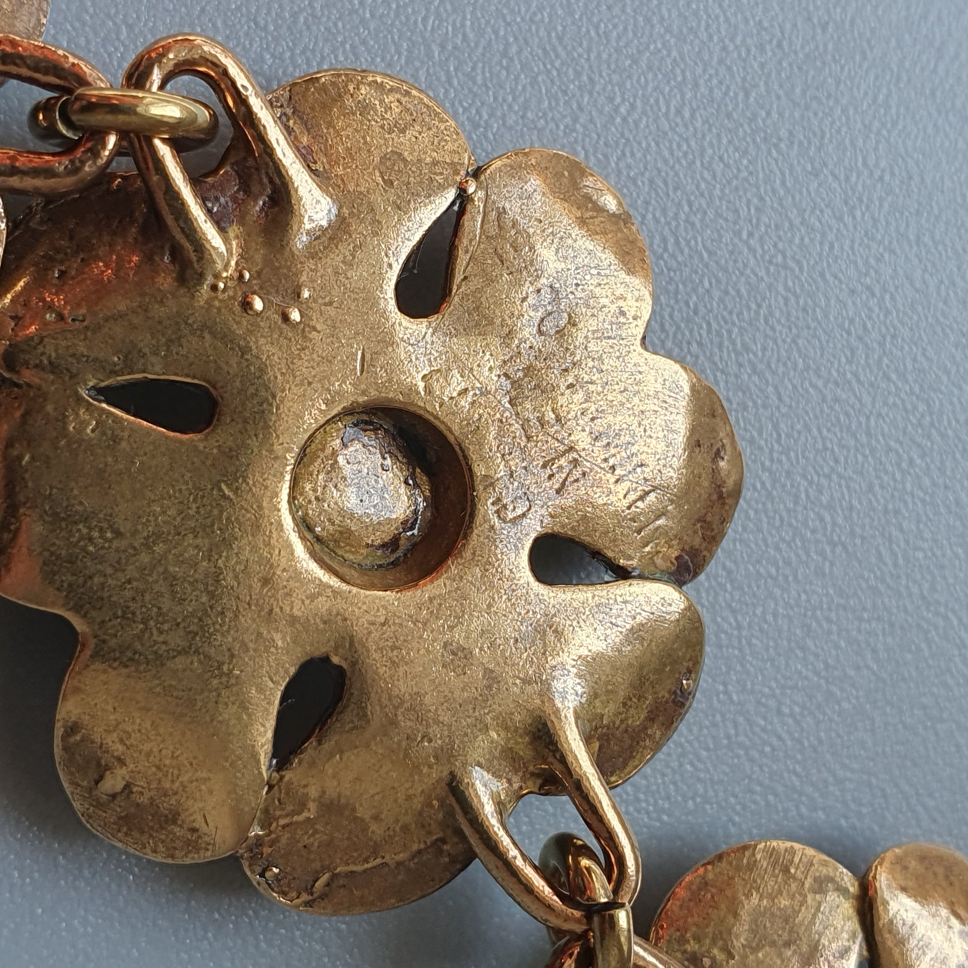 Ornate metal flower-shaped pendant or charm with multiple holes and a central indentation.