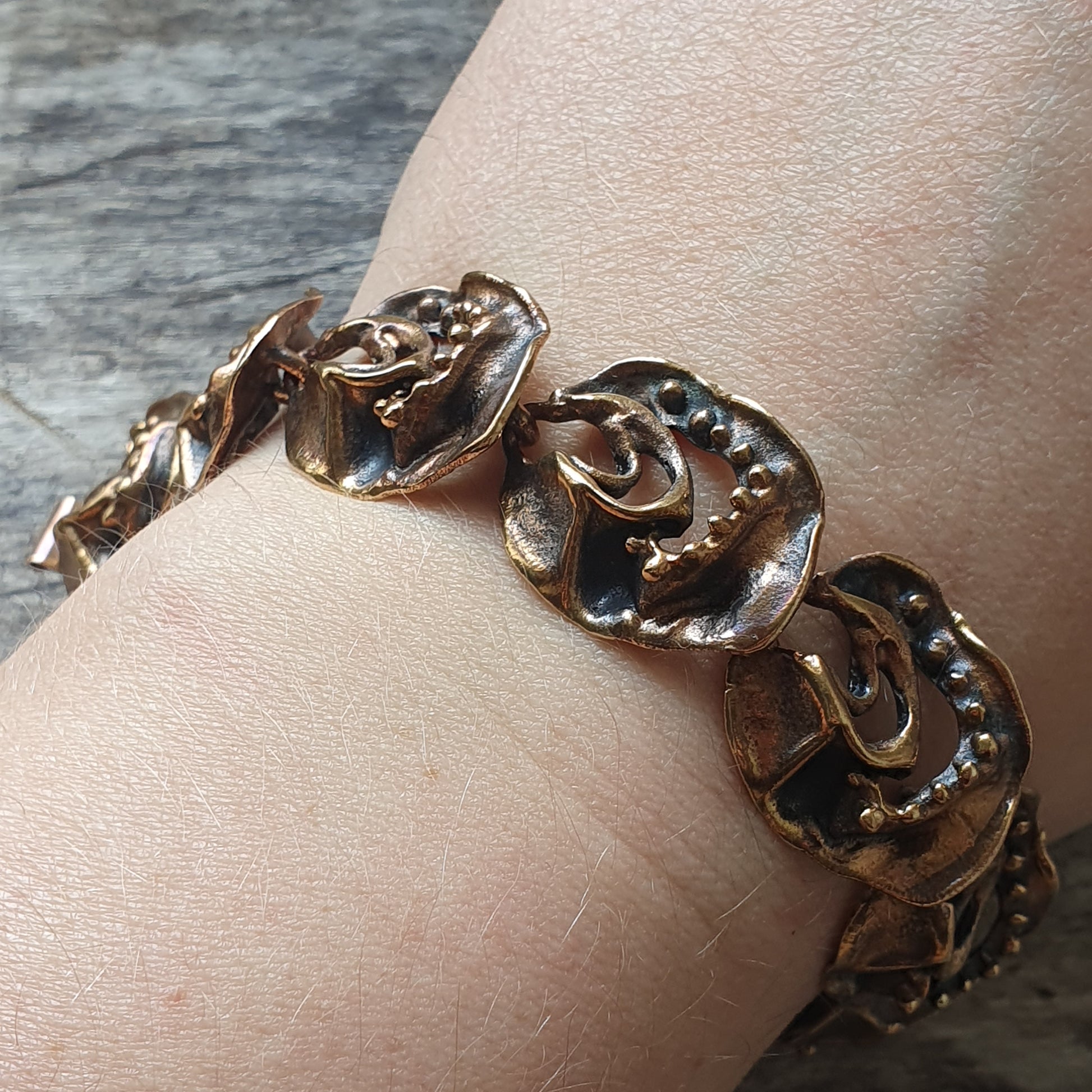 Gold-toned bracelet with abstract sculptural links worn on a wrist.