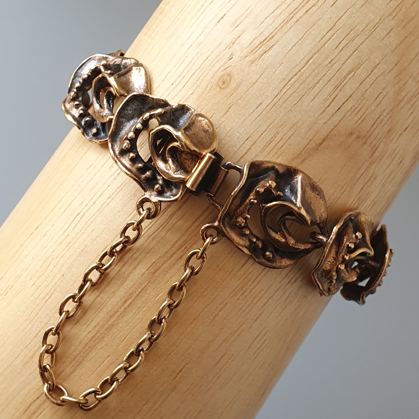 Antique-style gold bracelet with ornate floral or leaf-like designs and a safety chain.