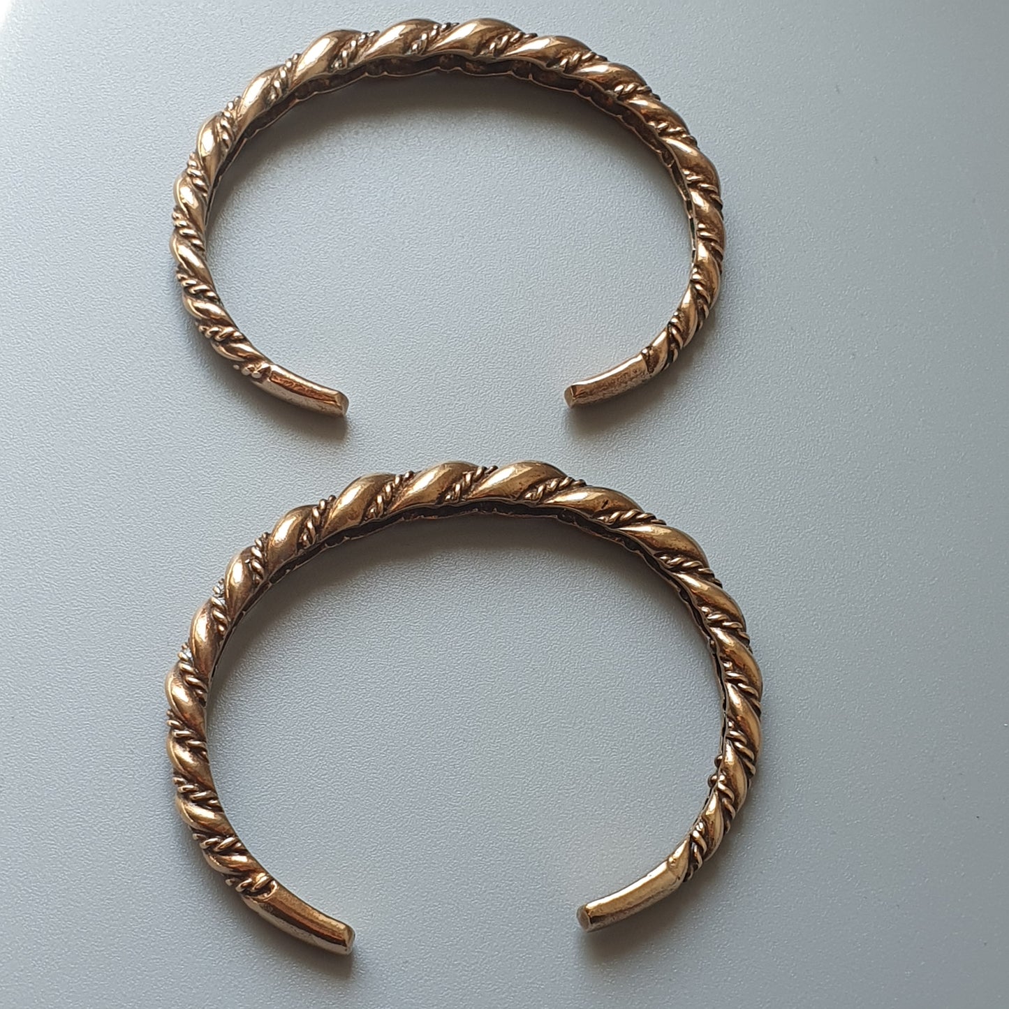 Two twisted gold-colored metal bracelets with open ends.