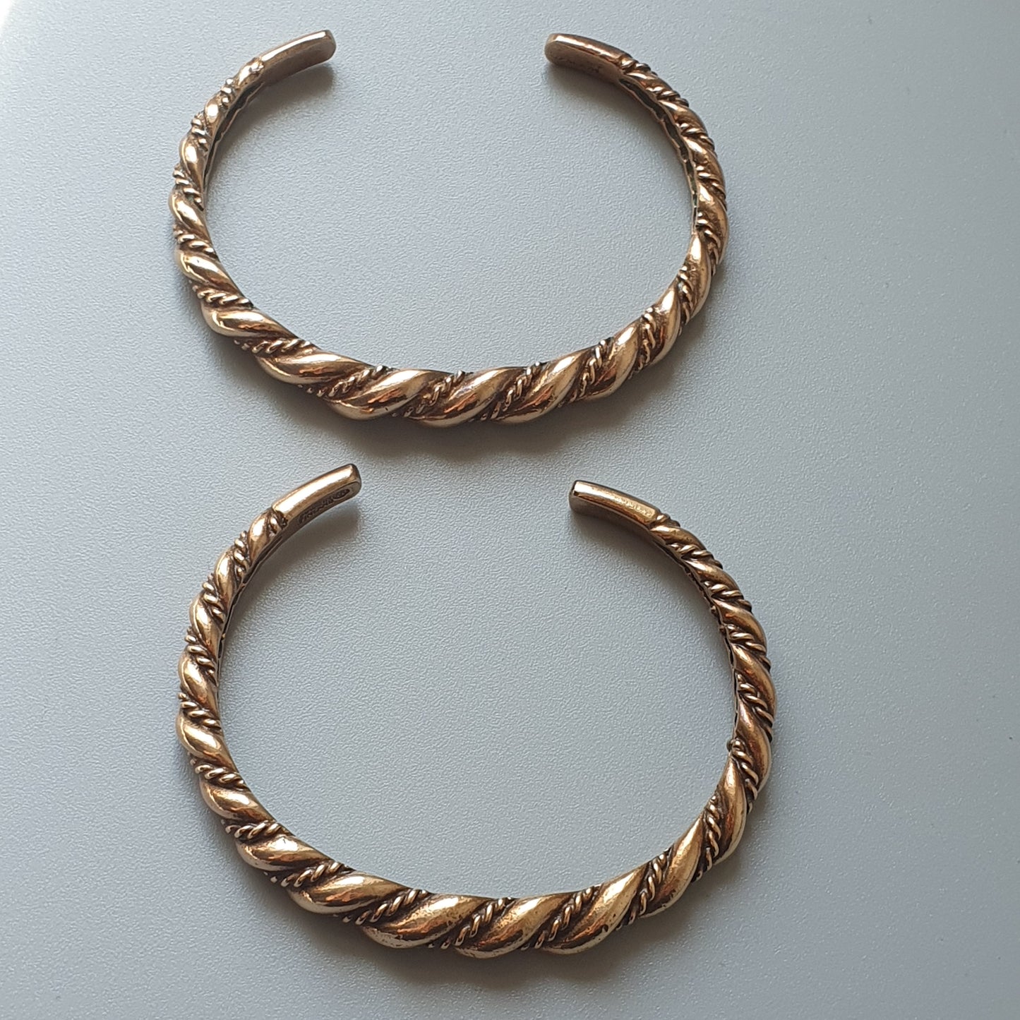 Two twisted gold-colored metal cuff bracelets with open ends.