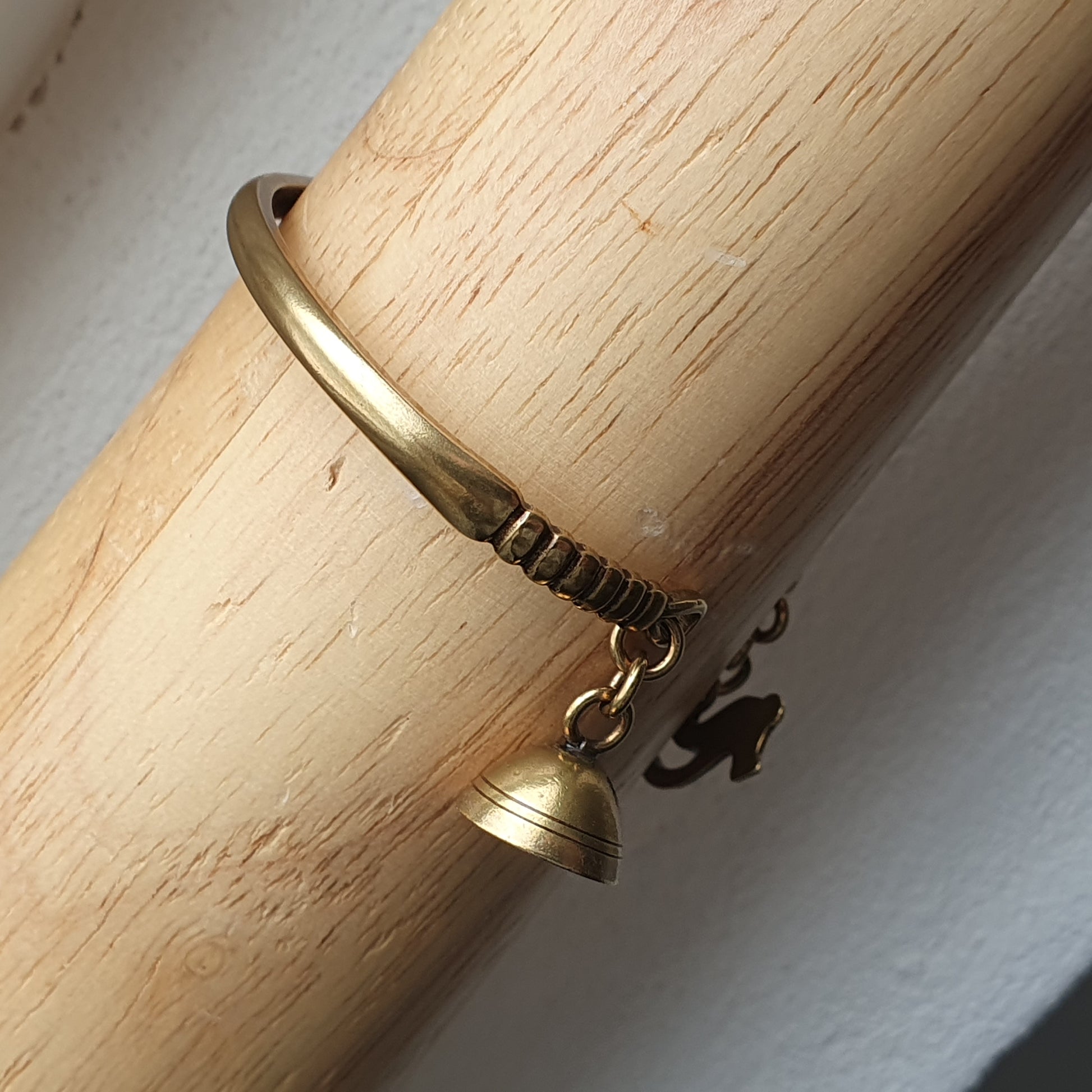 Gold bangle bracelet with a small bell charm attached.