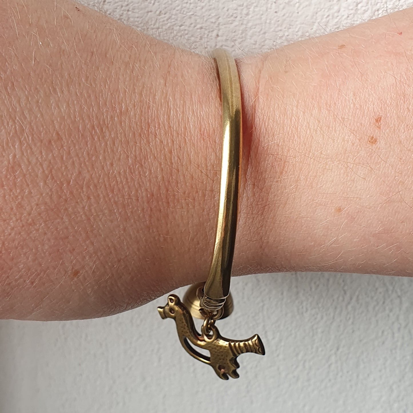 Gold bracelet with a dangling bird-shaped charm.