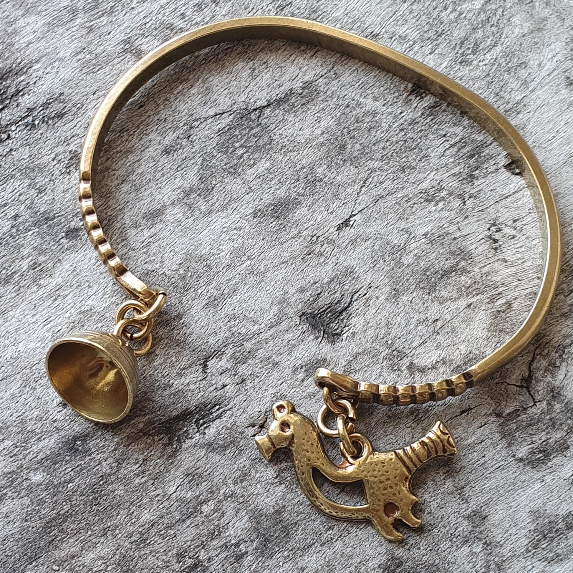 Gold-colored bracelet with dangling charms including a bell and a horse-like figure.