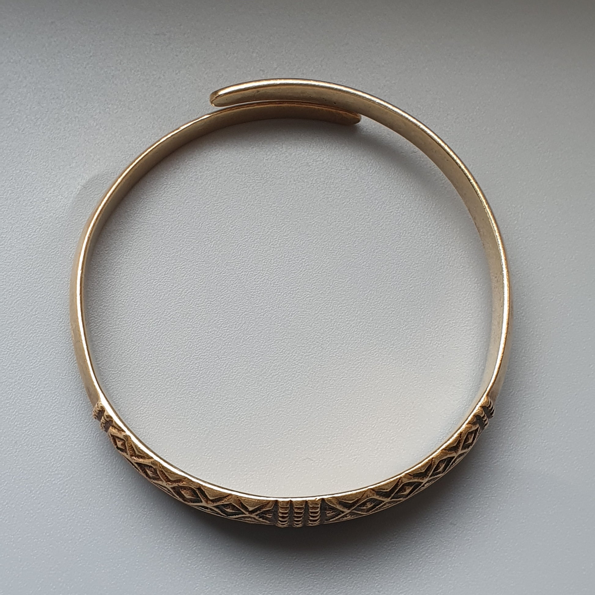 Gold bangle bracelet with intricate geometric patterns engraved on its surface.