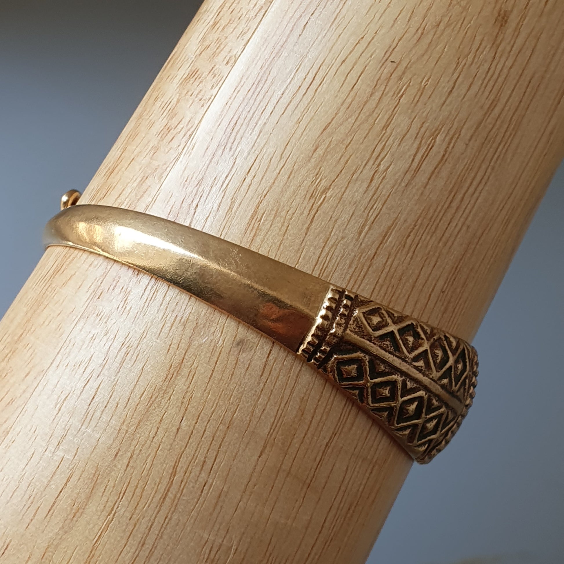 Gold bracelet with an intricate patterned end piece.