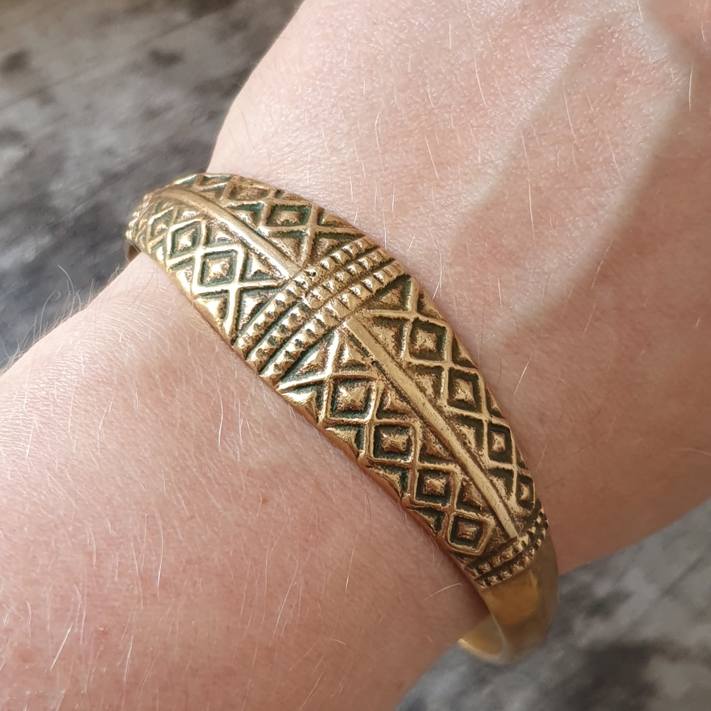 Gold bracelet with intricate geometric patterns worn on a wrist.