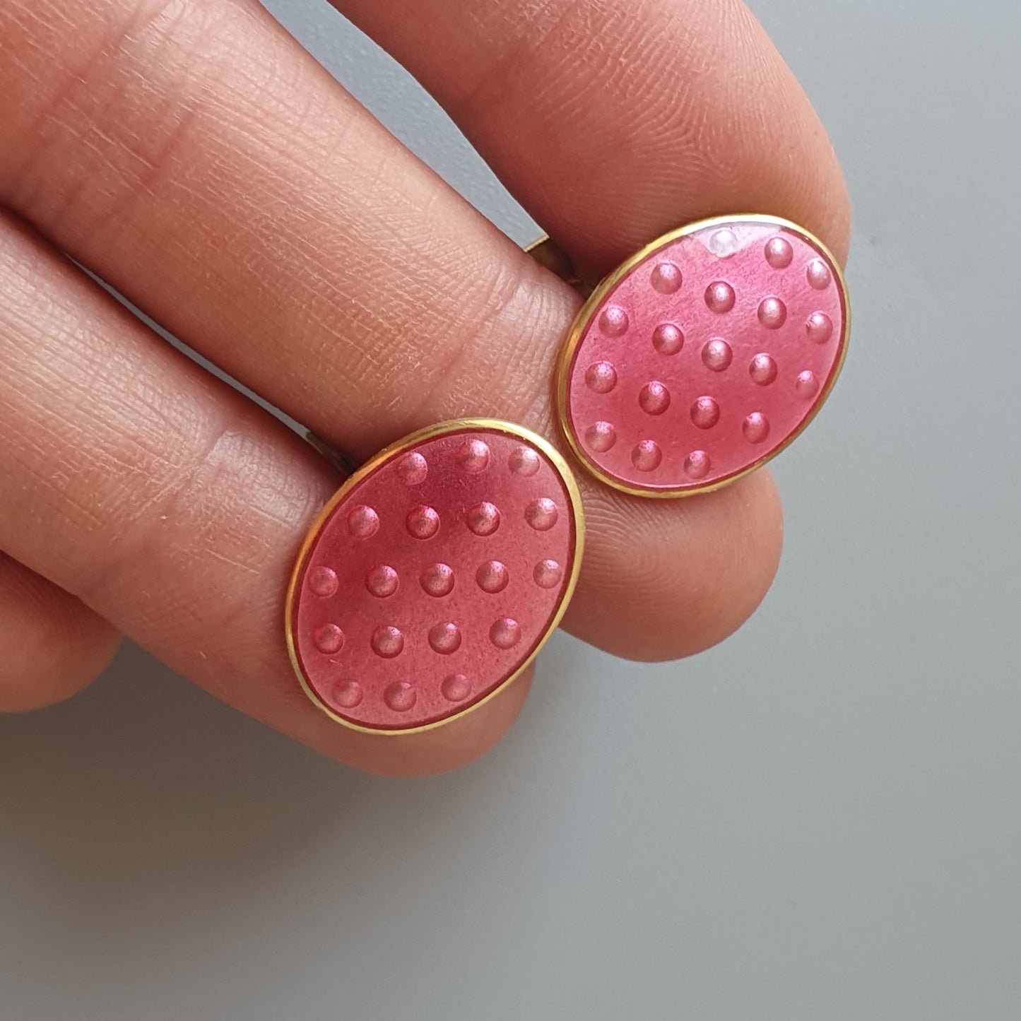 Pink oval earrings with raised dots and gold-colored edges.