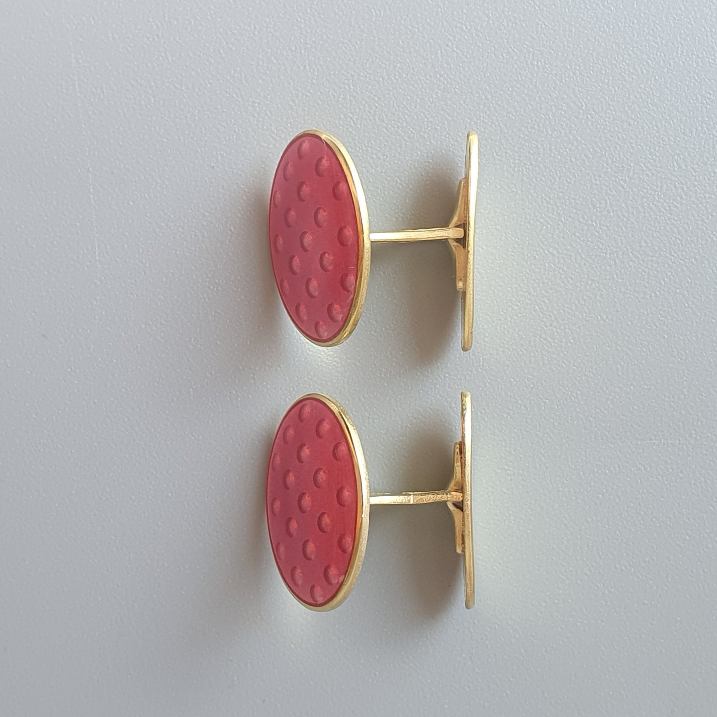 Pair of oval pink cufflinks with a textured surface and gold-toned metal settings.