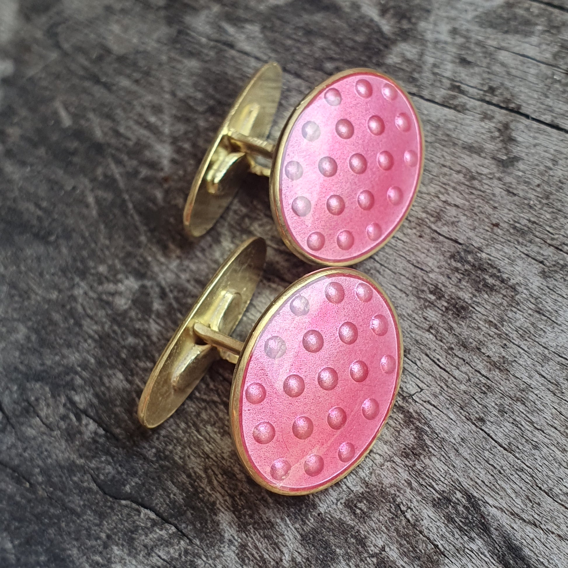 Pair of oval pink and gold cufflinks with a dotted pattern.