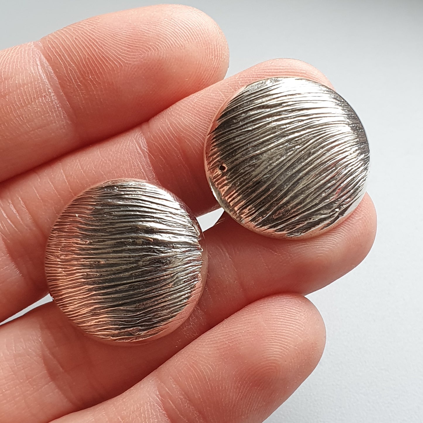 Pair of round, textured silver earrings held between fingers.