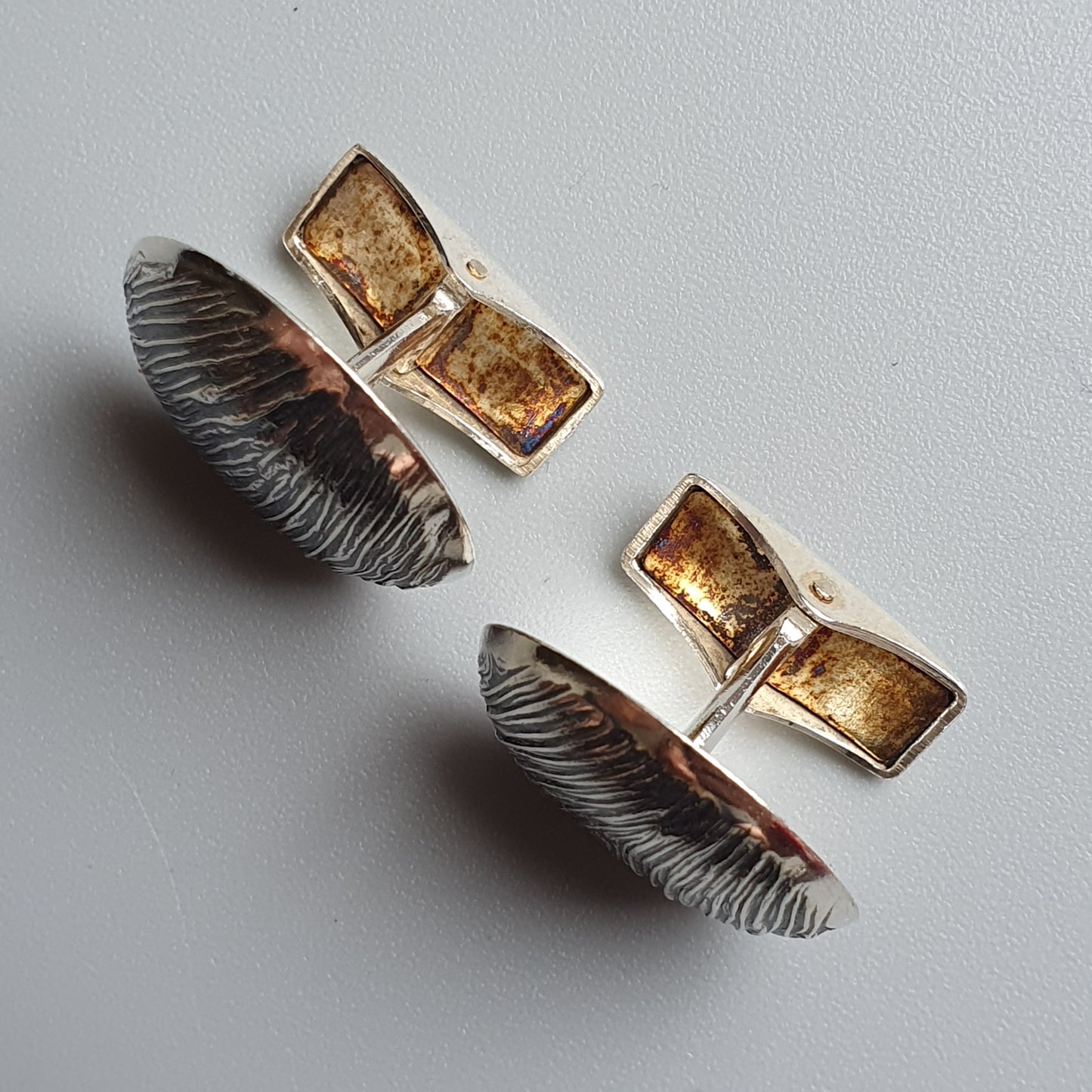 Pair of silver cufflinks with amber-colored stones and feather-like designs.