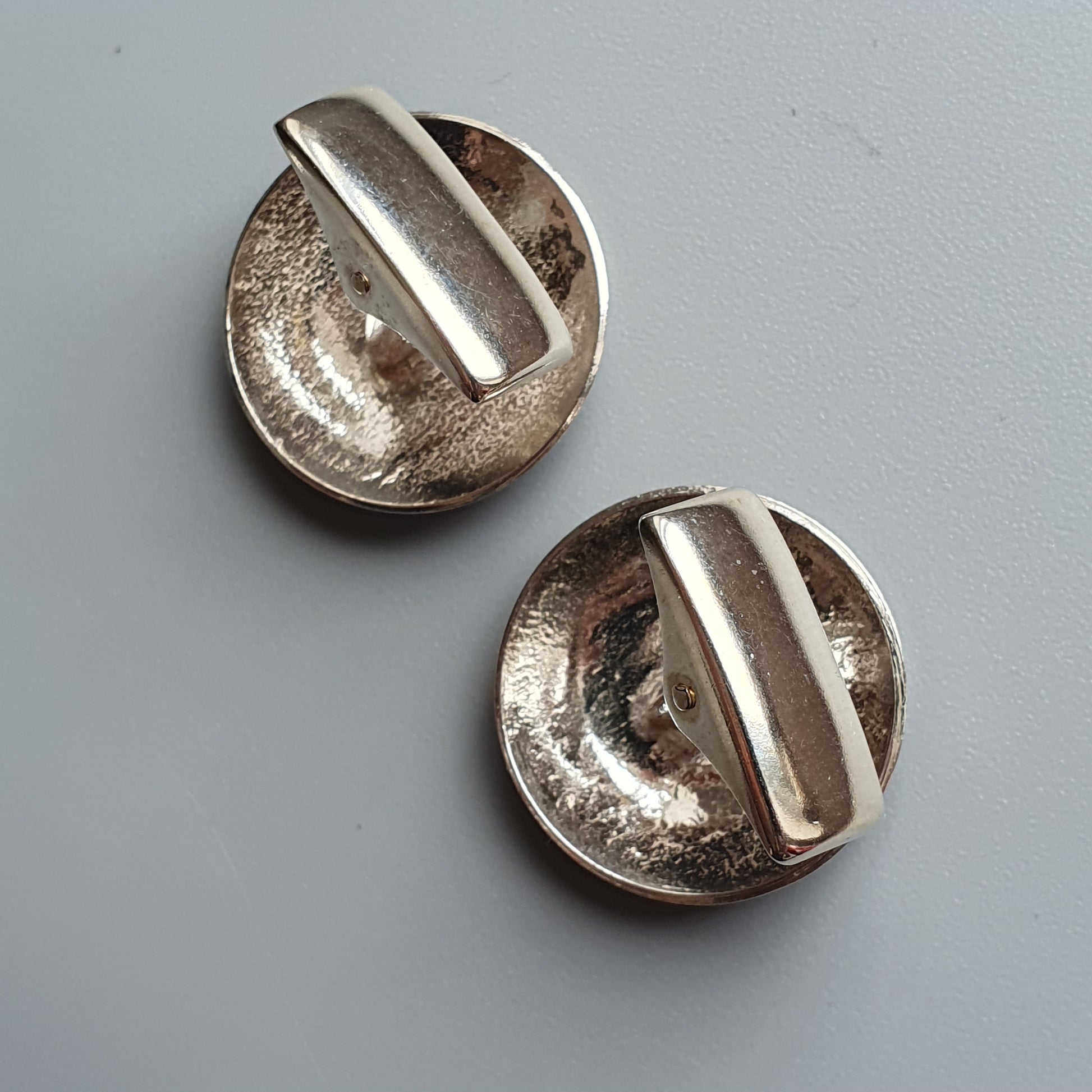 Two round silver buttons with raised linear designs across their centers.