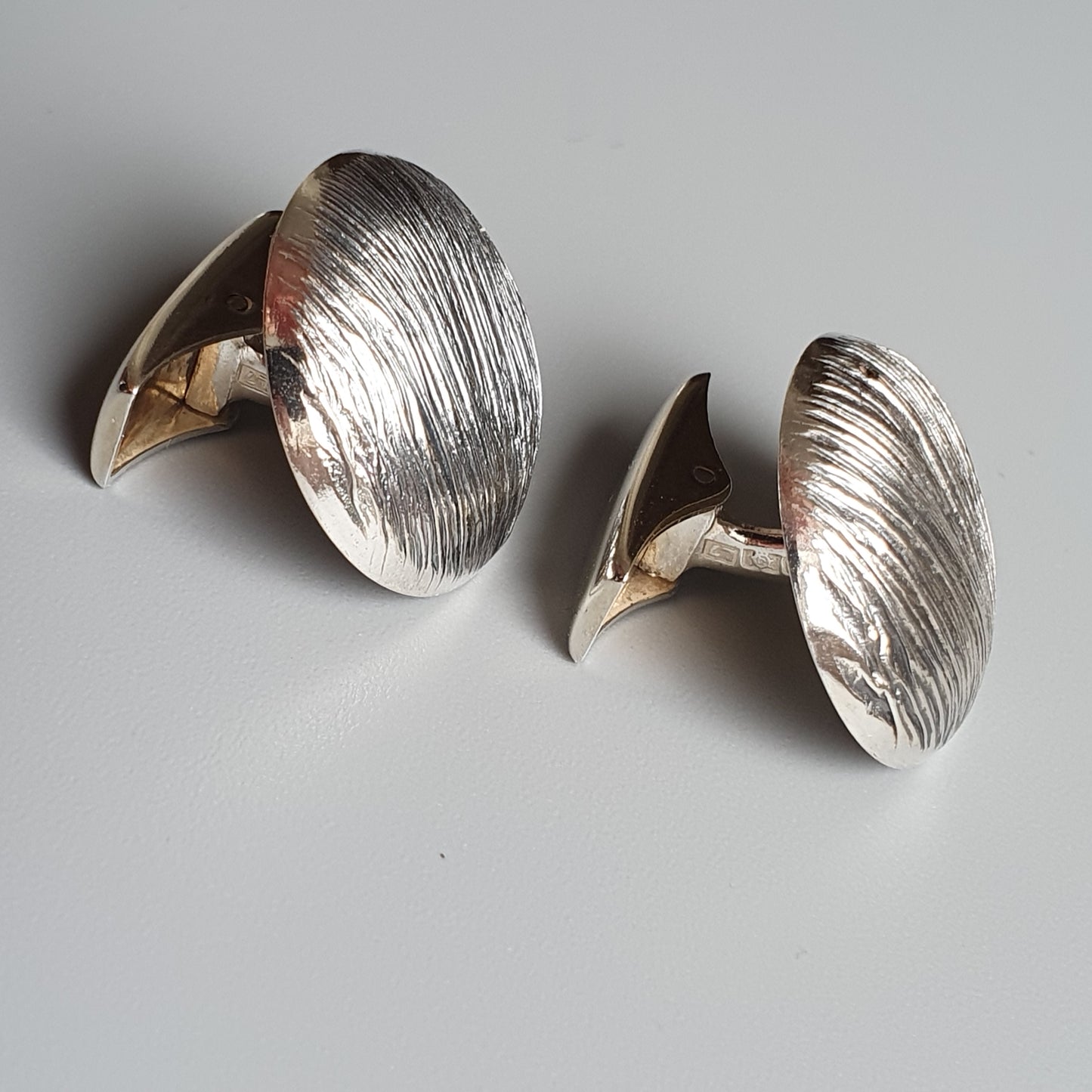 Pair of oval-shaped silver cufflinks with textured surfaces.