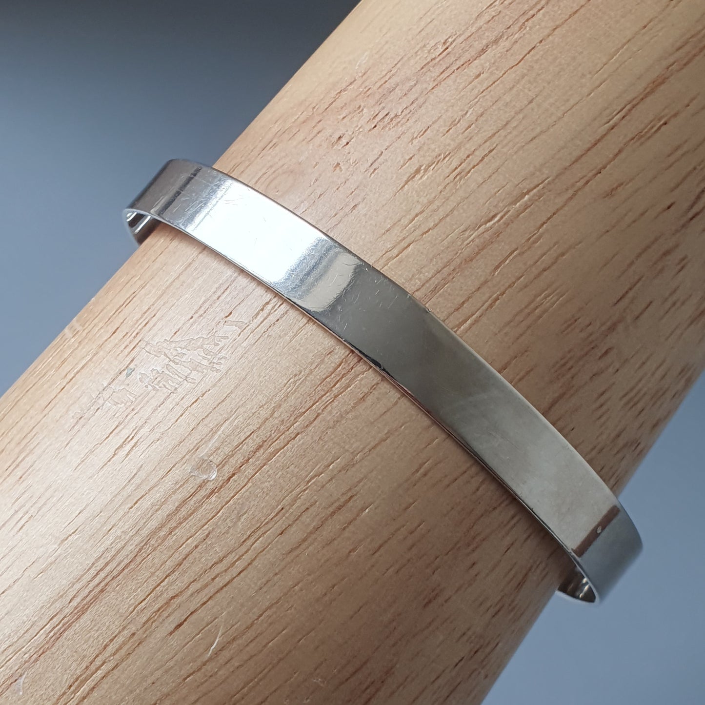 Silver metal bracelet or bangle wrapped around a wooden cylinder.