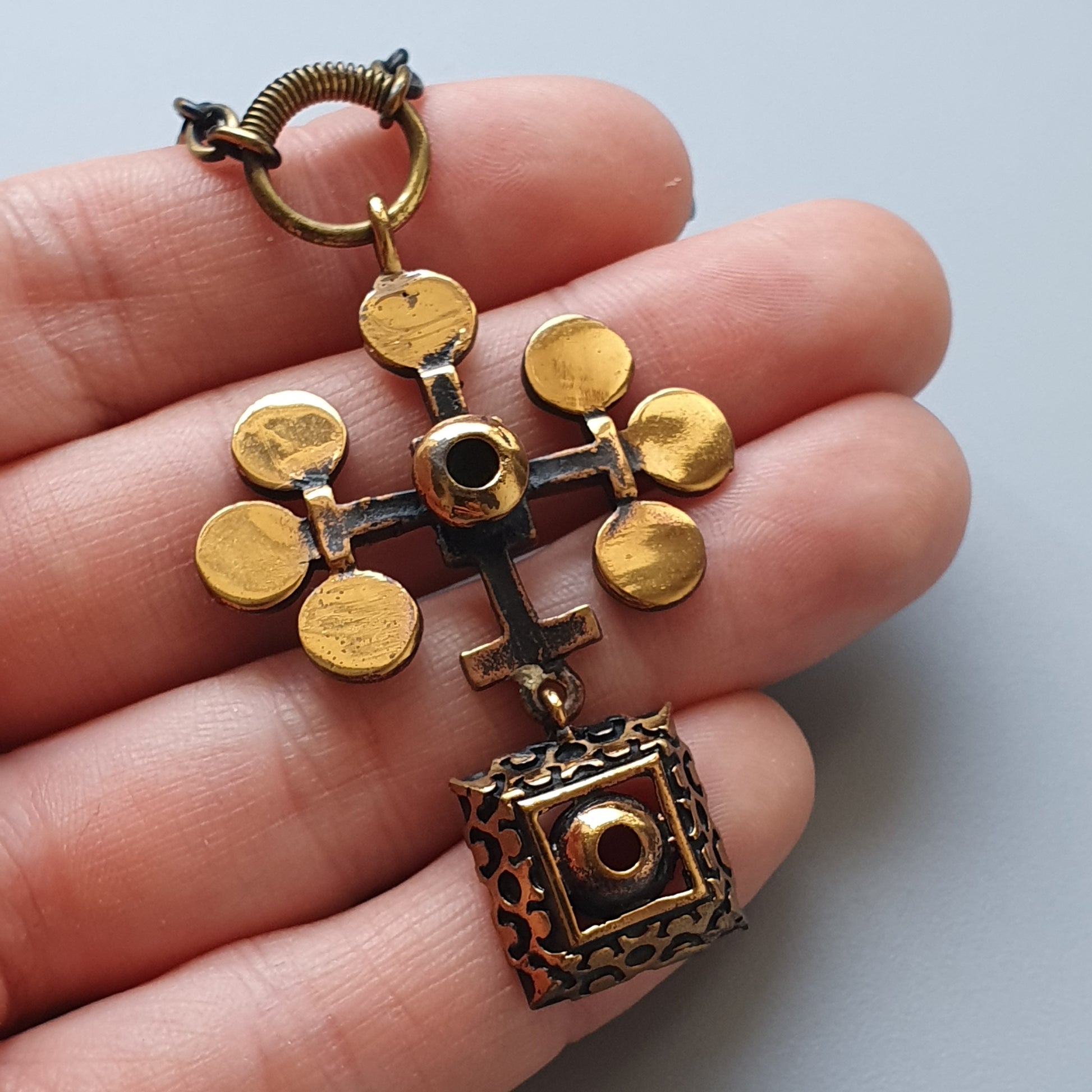 Ornate cross pendant with golden circular attachments and a decorative cube at the bottom.