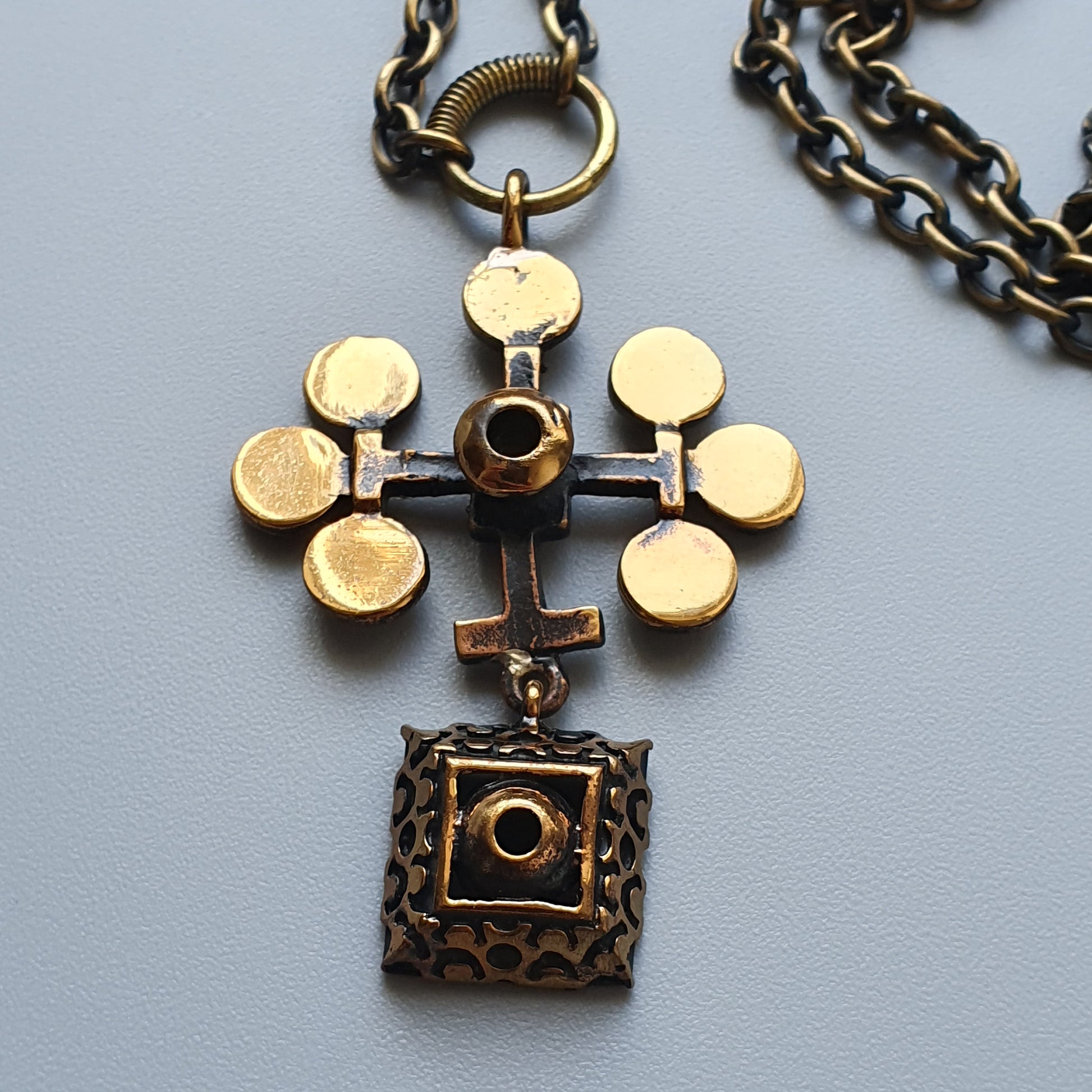 Ornate pendant necklace featuring a cross-like design with circular elements and a square charm.