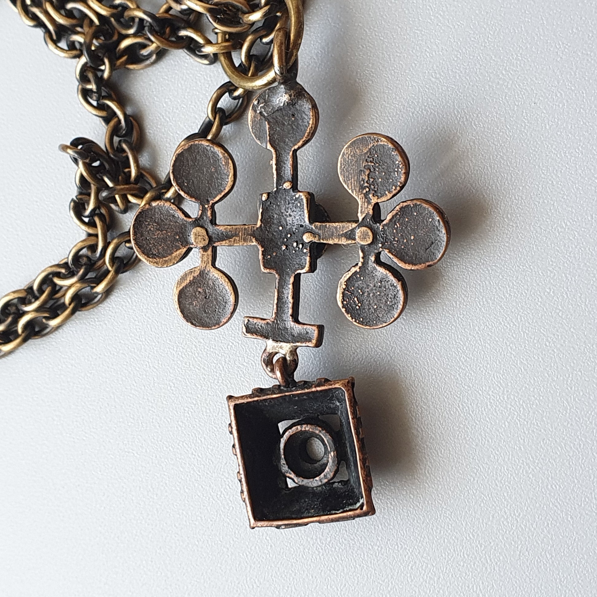 Ornate metal cross pendant with a small square attachment hanging from a chain.