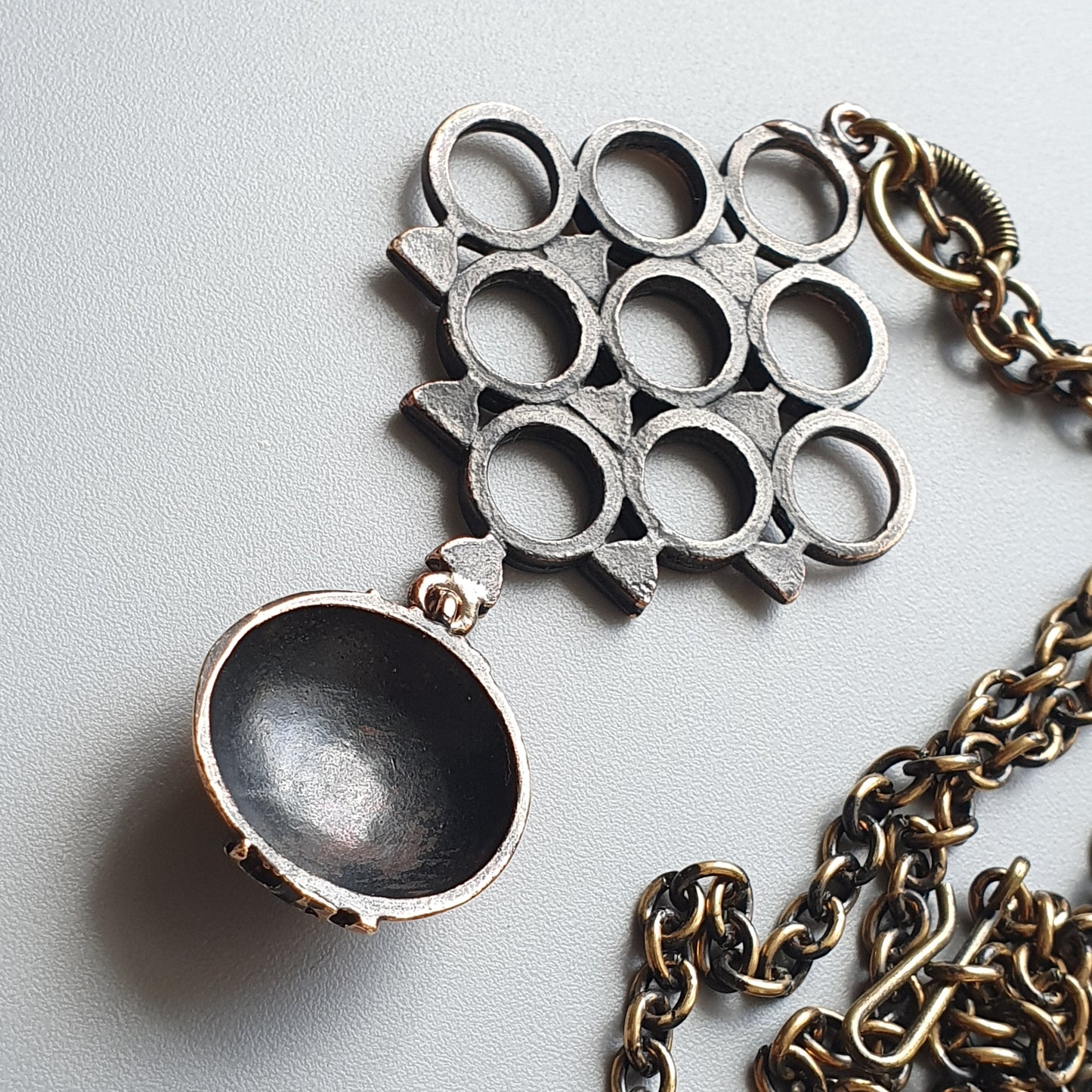 Metallic pendant necklace with a grid-like pattern and an oval charm attached to a chain.