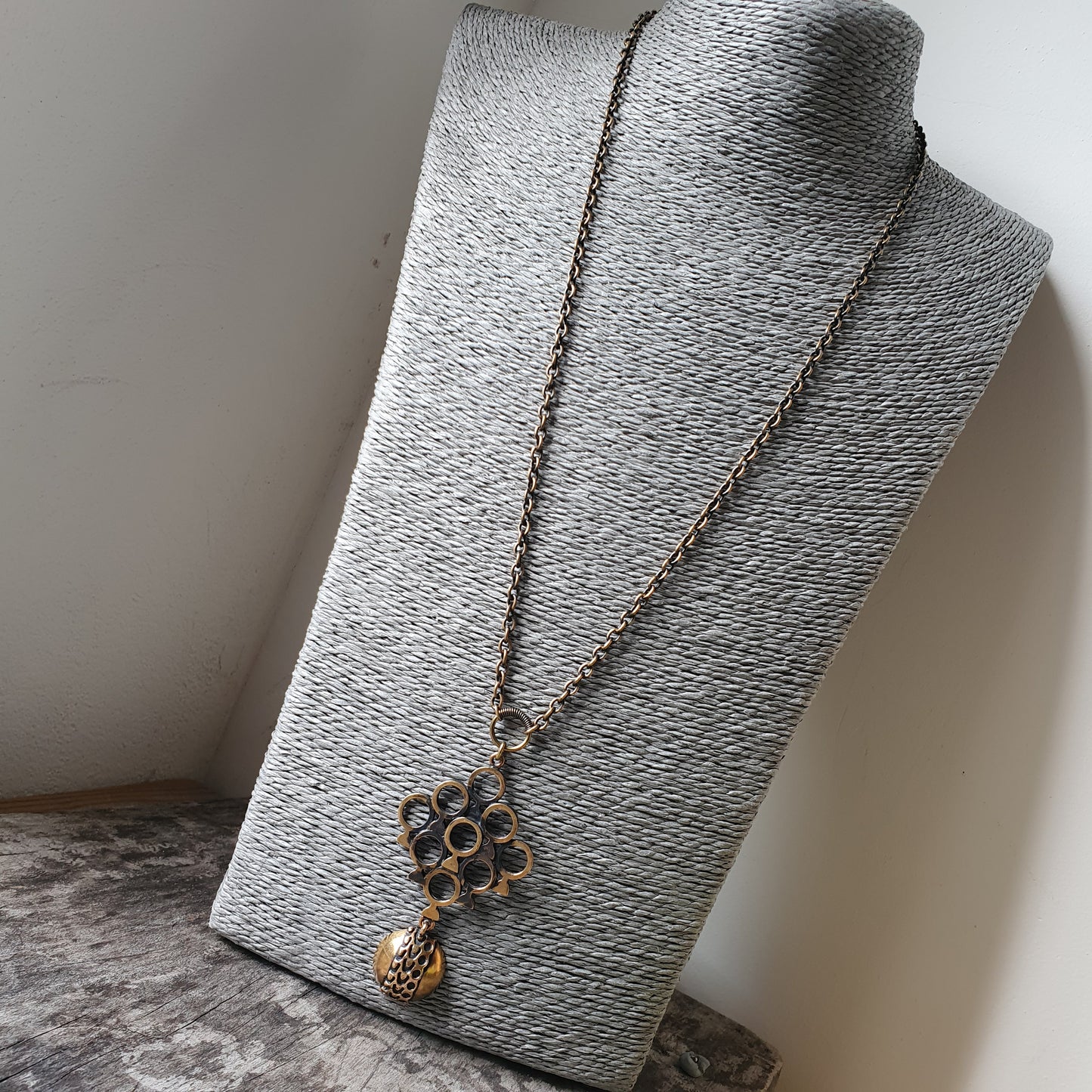 Necklace with a floral pendant and dangling charm on a textured display stand.