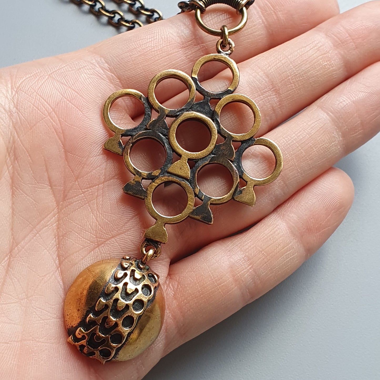 Brass pendant necklace with circular openwork design and dangling amber-colored stone.