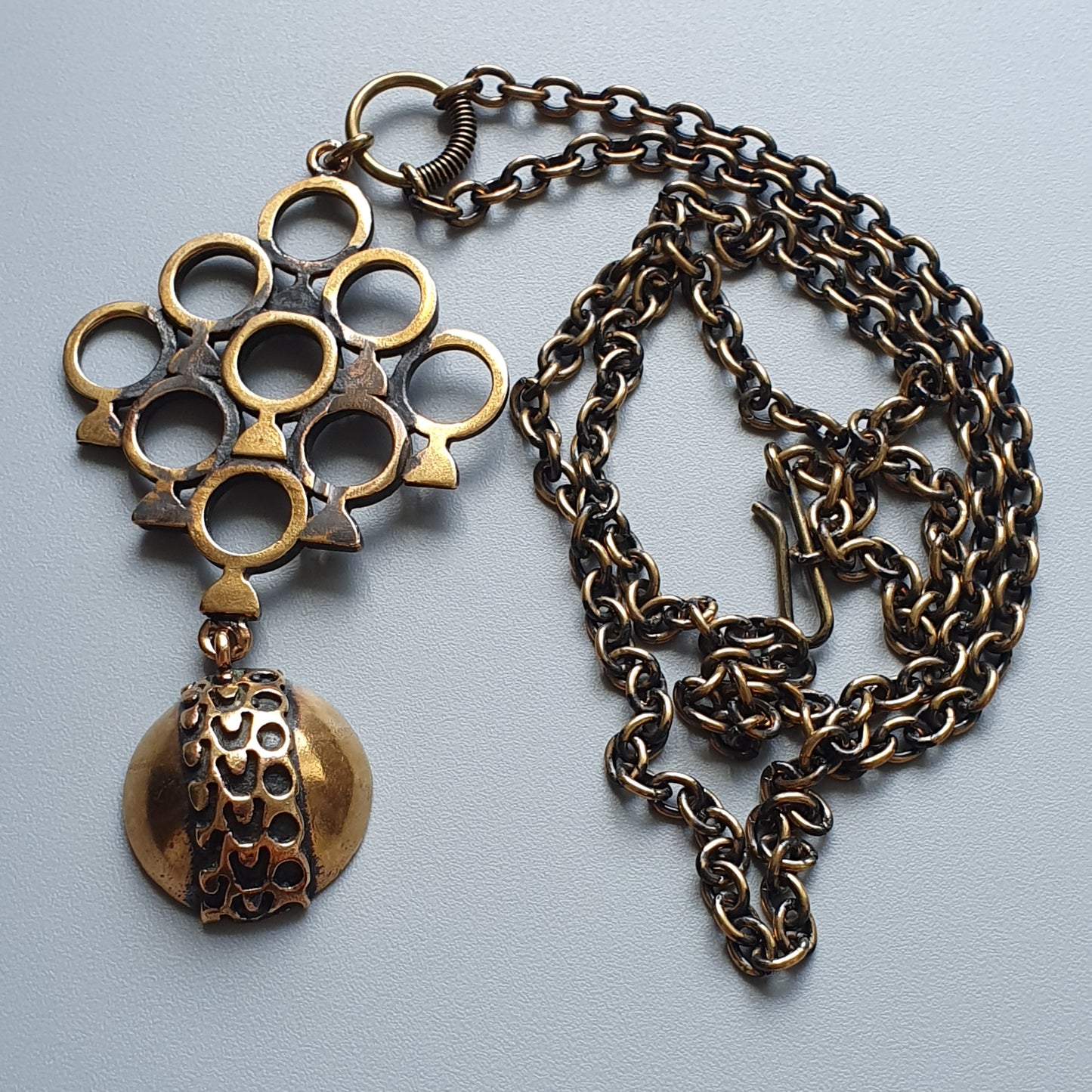 Vintage-style pendant necklace with a circular geometric design and dangling ornament.