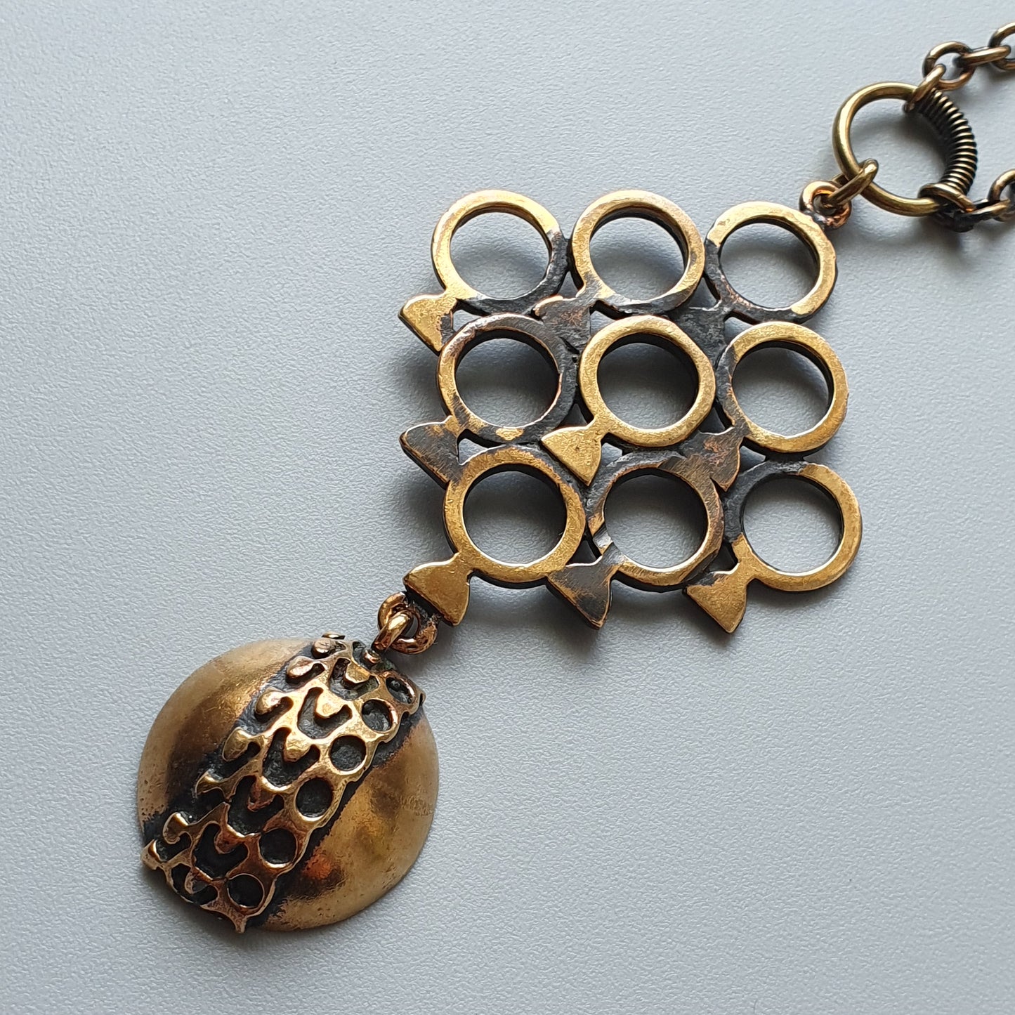 Ornate metal pendant featuring a grid of circles and a dangling spherical charm.