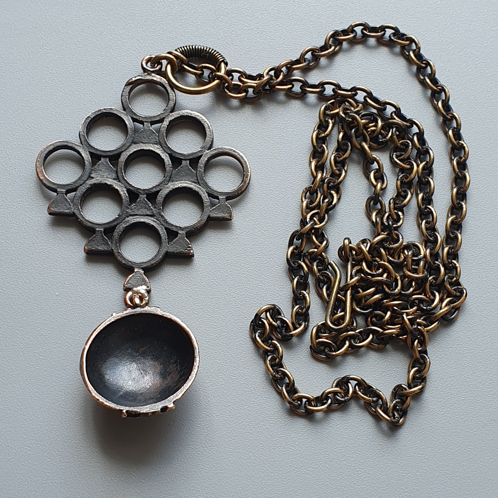 Metallic pendant necklace featuring a circular knuckle duster design and a small bowl-shaped charm.