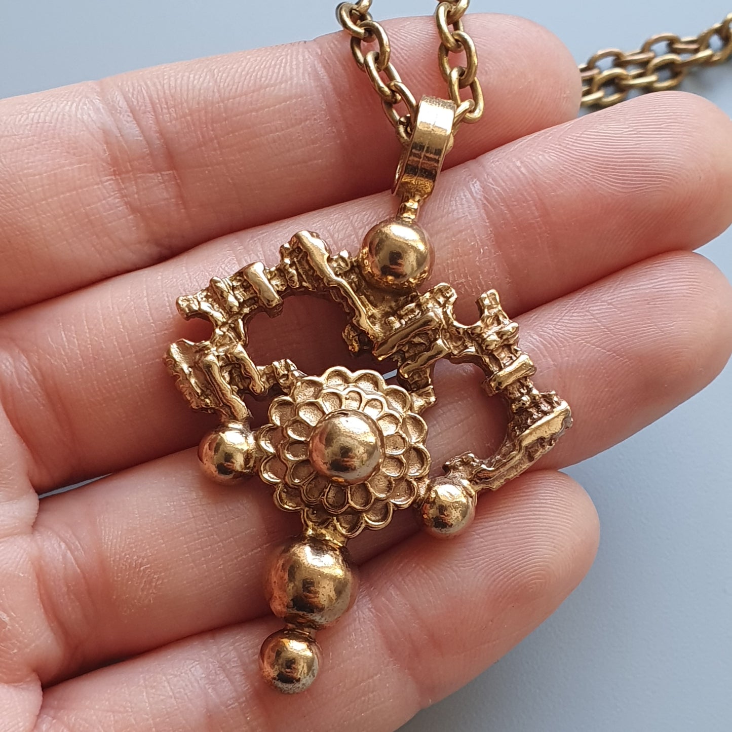 Gold-colored pendant necklace featuring an intricate design with spherical elements and a floral-like central motif.