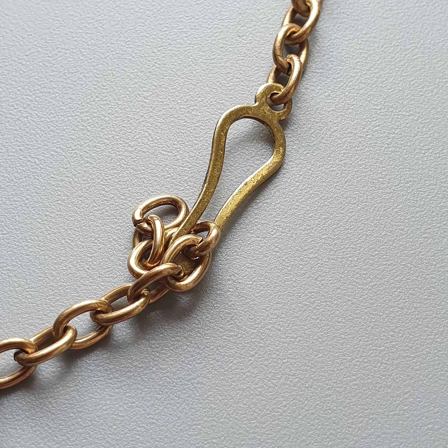 Gold-colored metal clasp or hook attached to a chain.