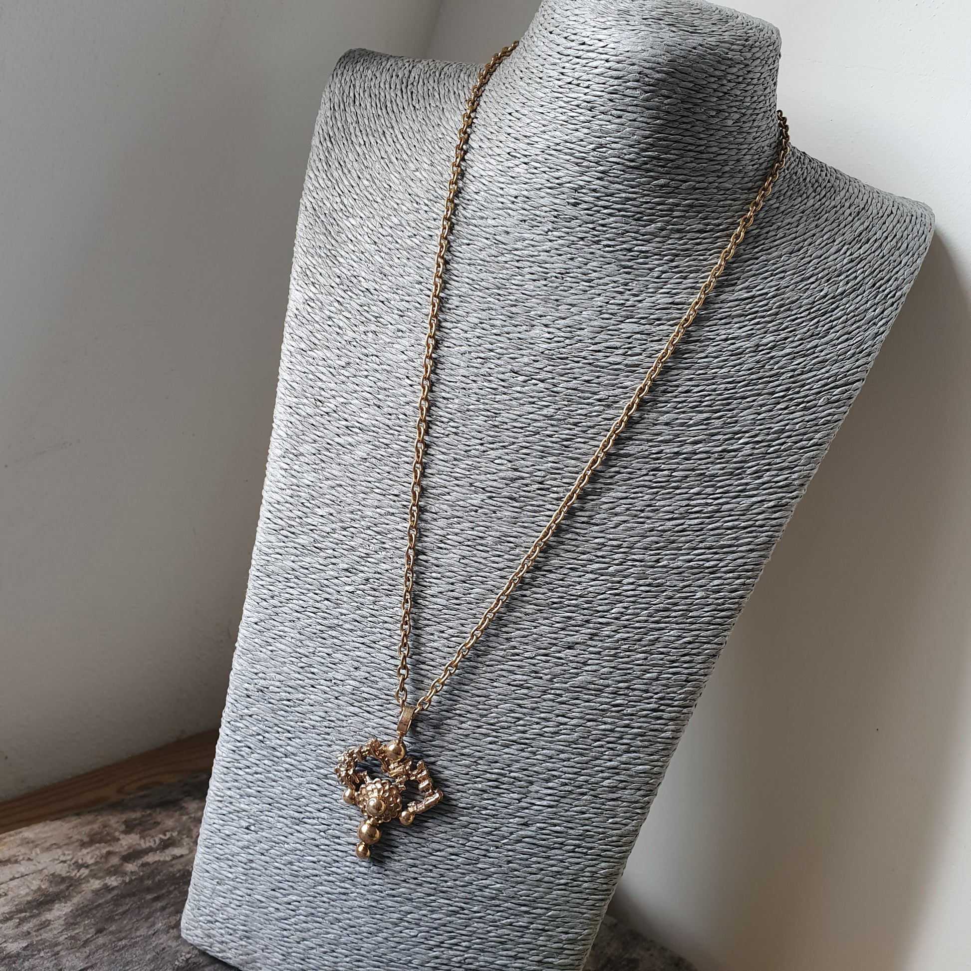 Gold-toned necklace with a cross pendant displayed on a gray jewelry bust.