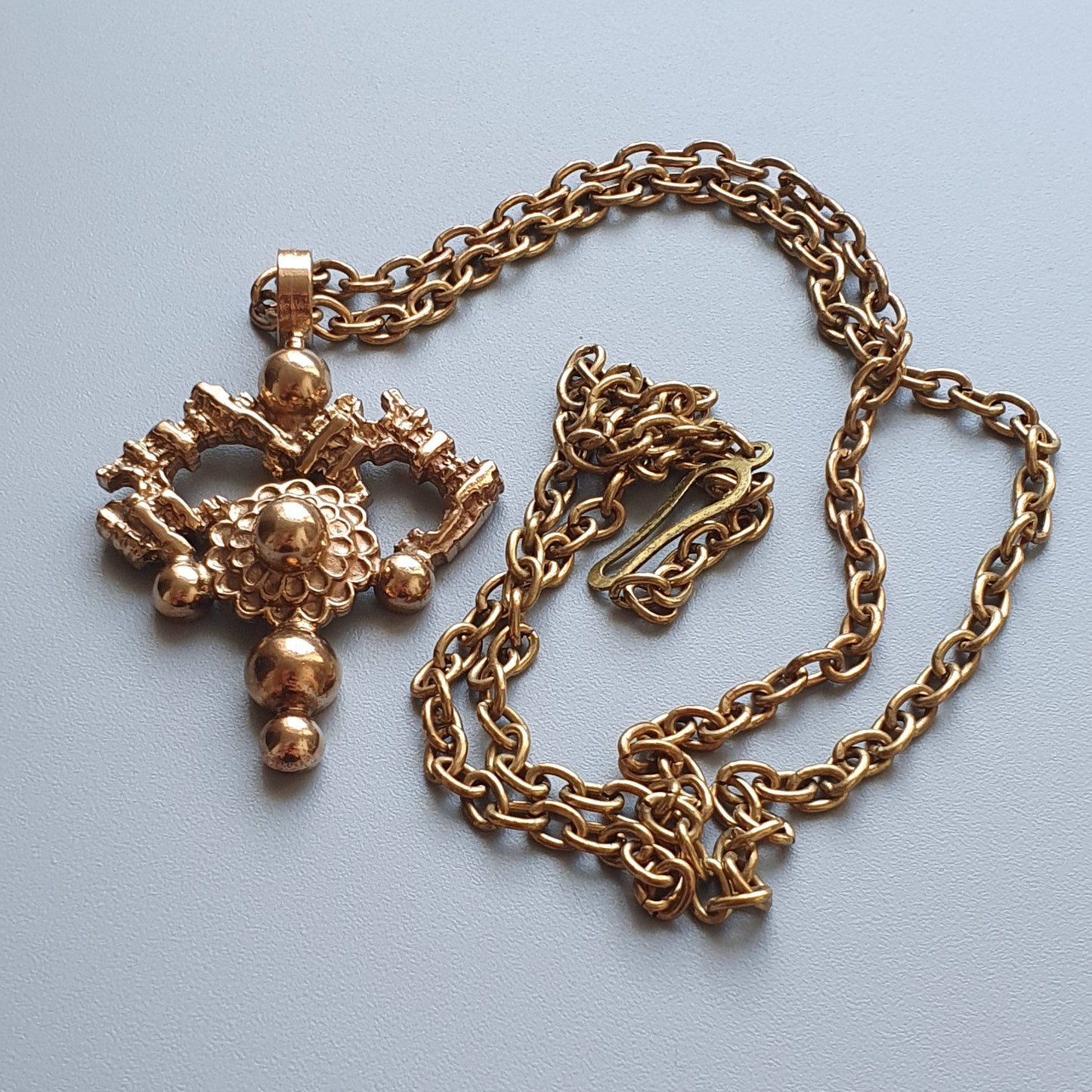 Ornate gold-colored pendant necklace with an intricate cross-shaped design.