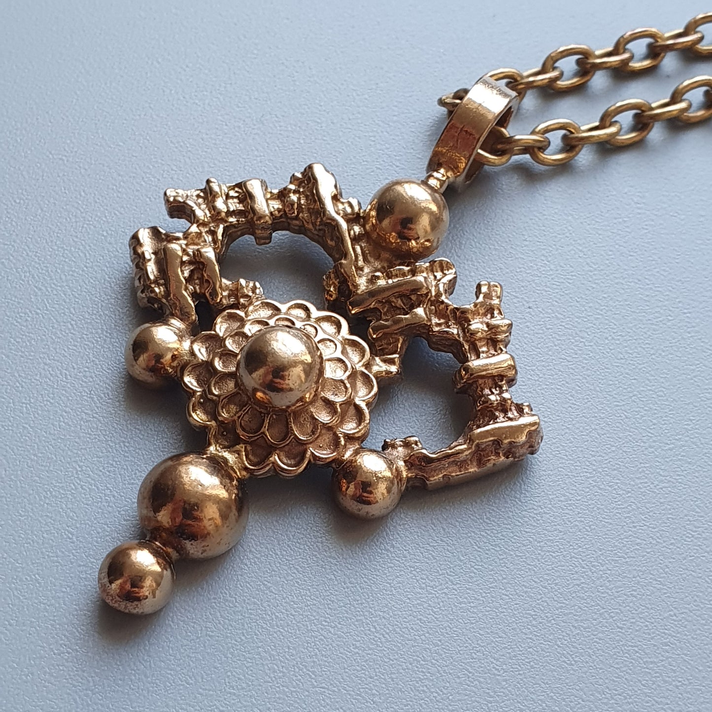 Gold-toned pendant necklace featuring an intricate design with spherical elements and architectural motifs.