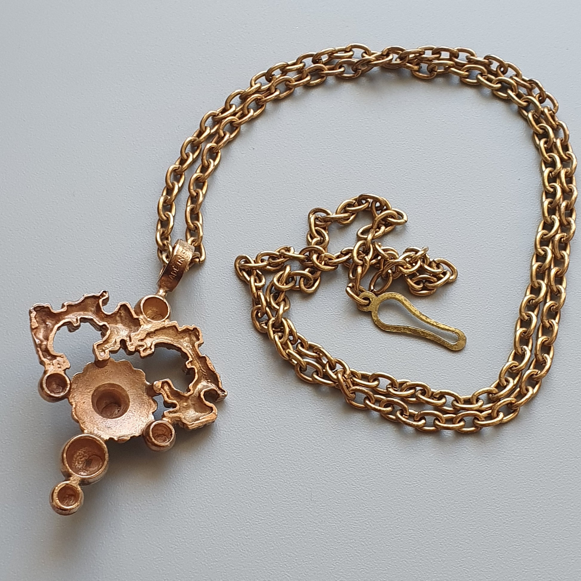 Gold-toned chain necklace with an ornate, abstract pendant featuring circular shapes.