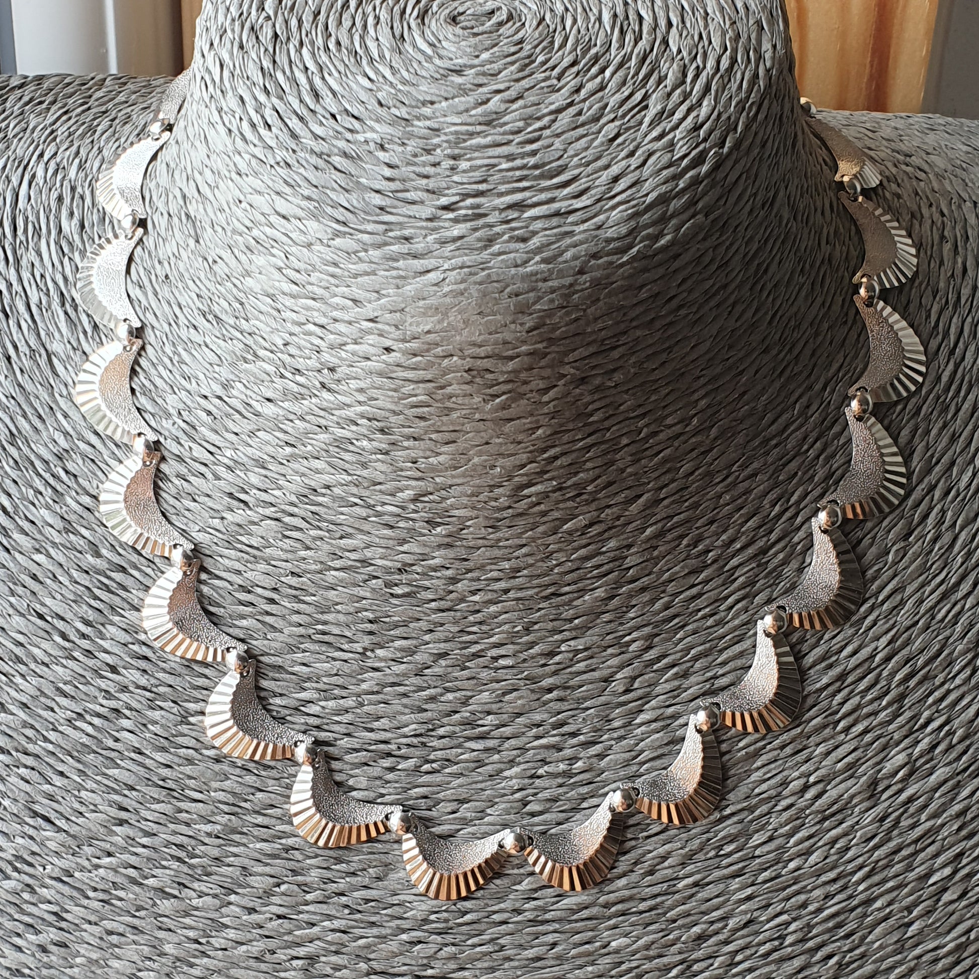 Delicate silver necklace with scalloped shell-like design displayed on a textured gray surface.