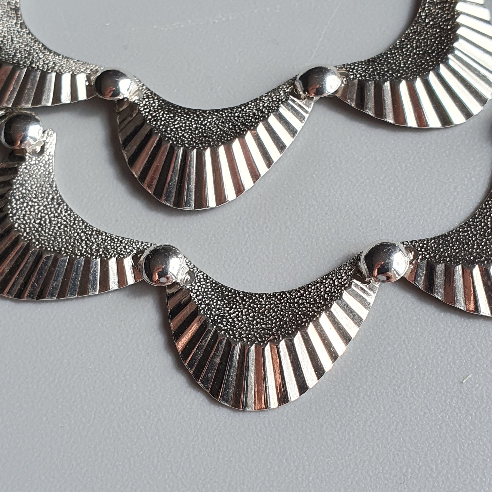 Ornate silver necklace with scalloped, textured segments and smooth curved elements.