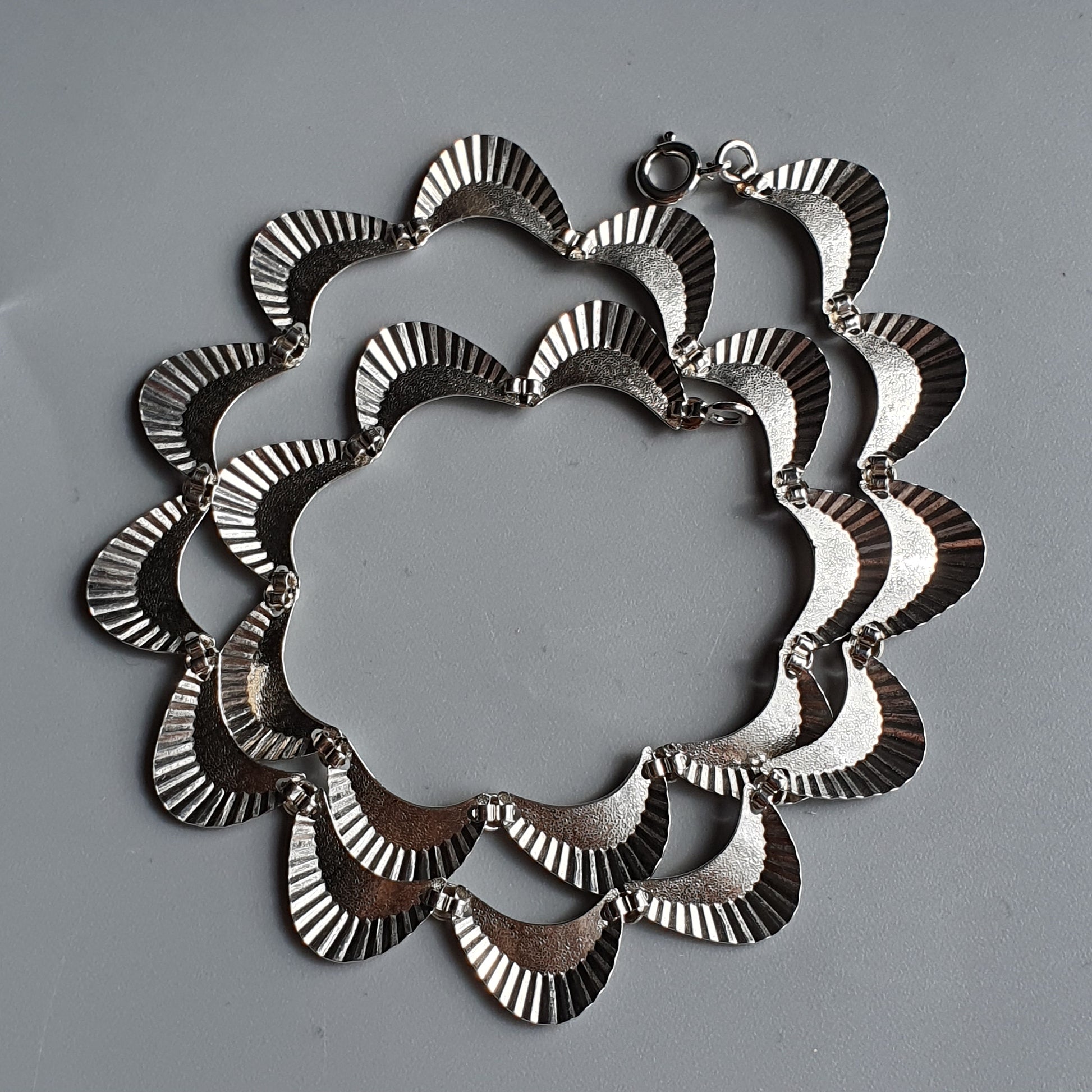 Silver necklace with a scalloped, floral-like design made of overlapping curved segments.