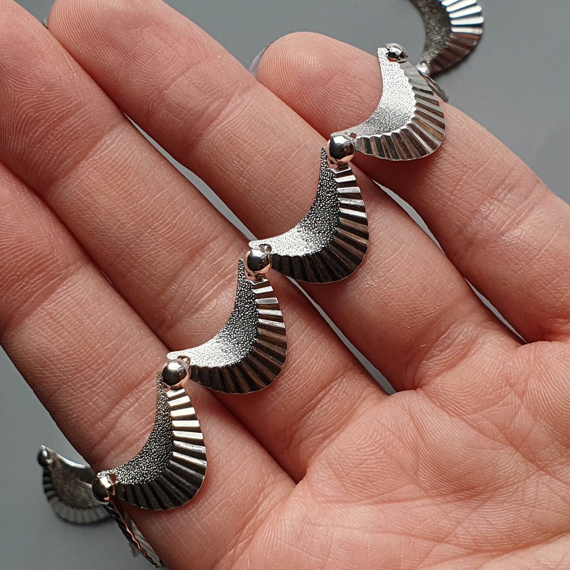 Metallic spiral-shaped bracelet with fan-like segments resting on an open palm.