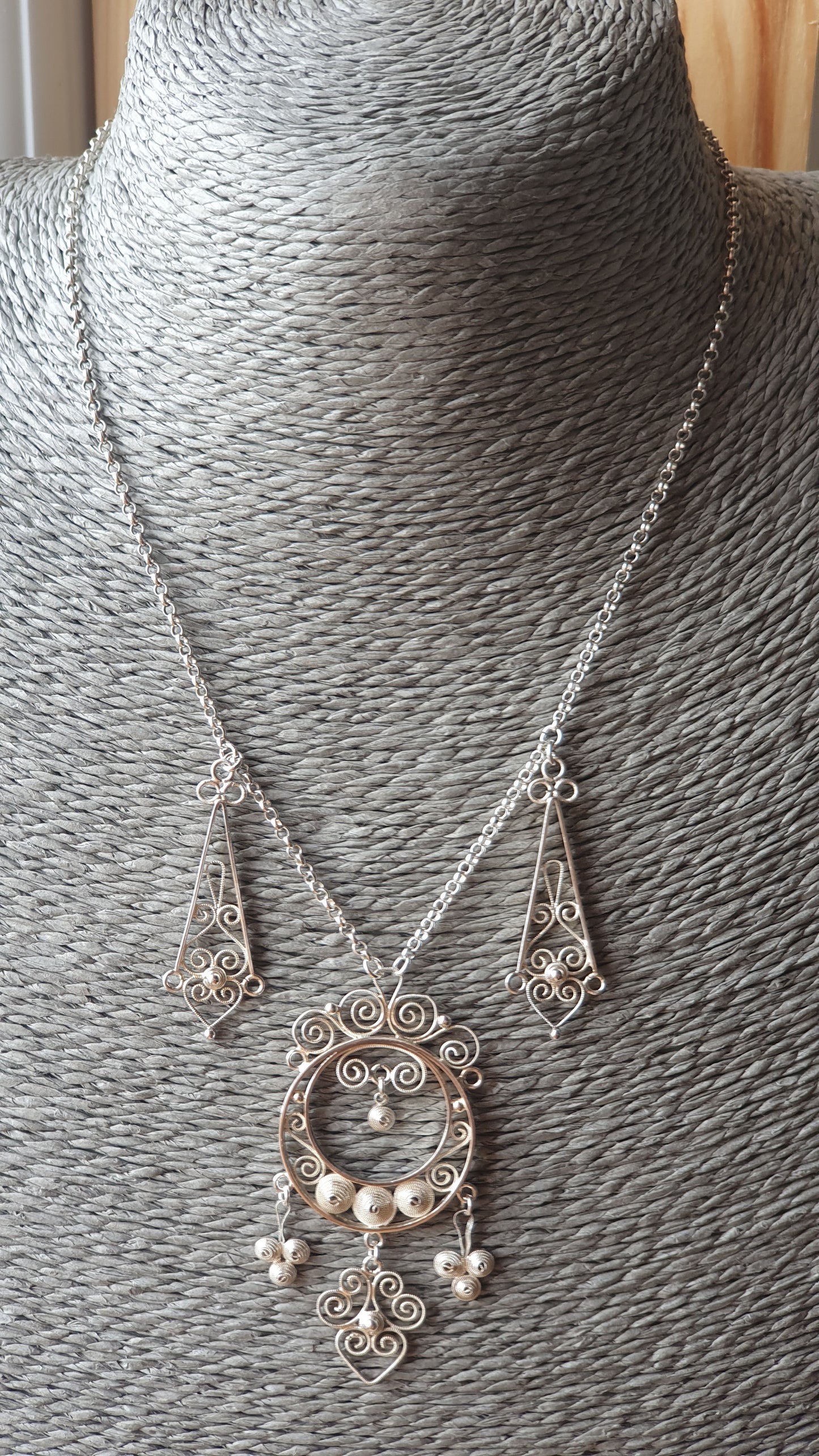 Ornate silver necklace with a pendant featuring intricate filigree and dangling elements.