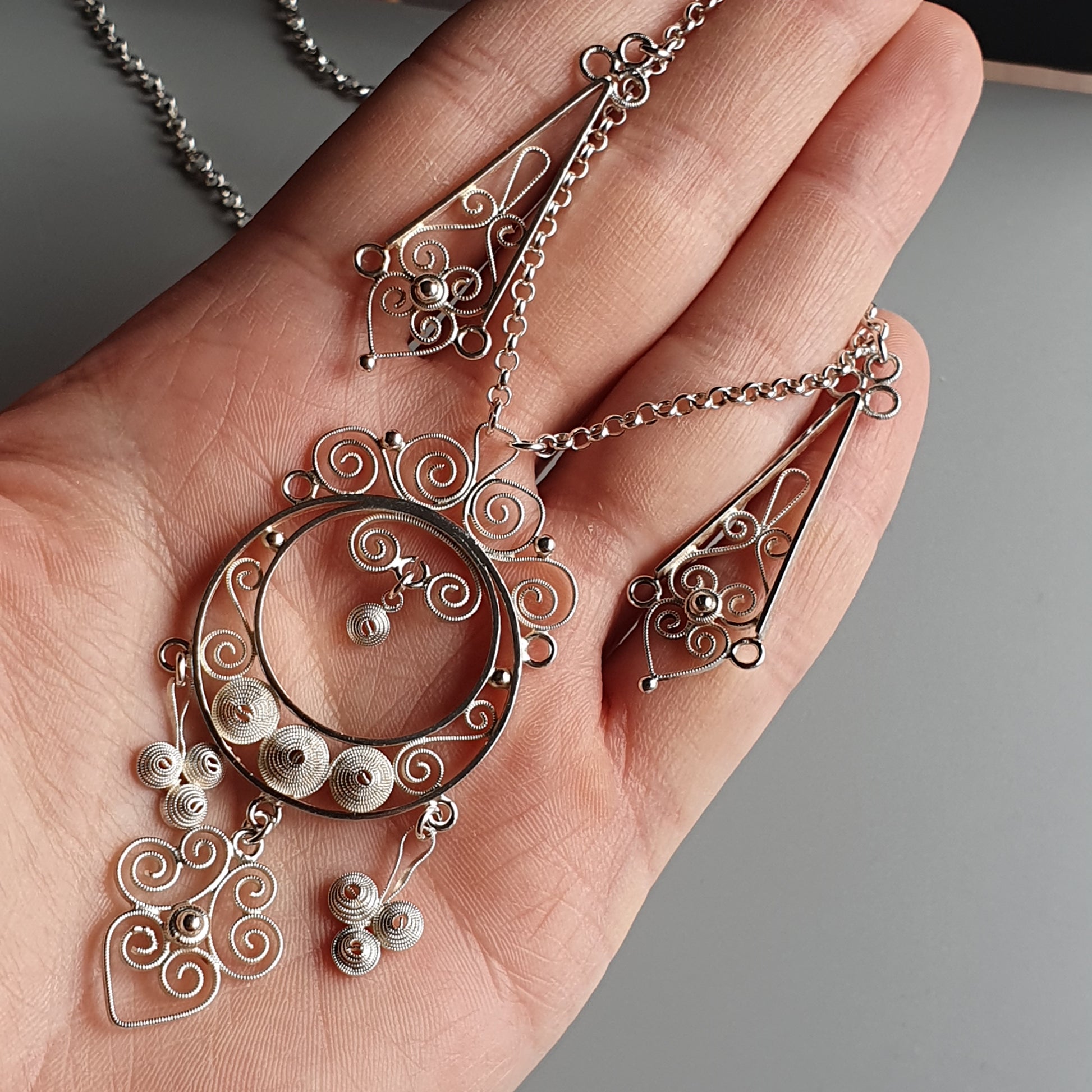 Ornate silver pendant necklace with swirling filigree designs and small dangling elements.