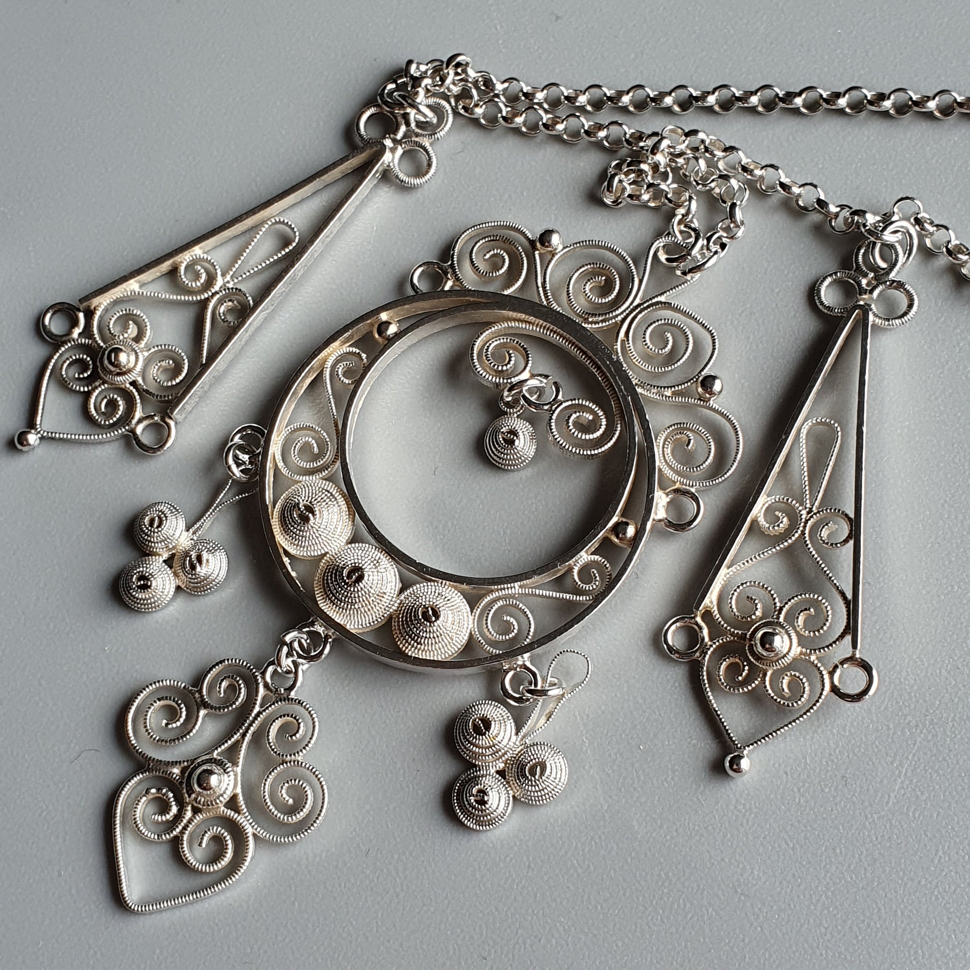 Ornate silver filigree necklace with circular pendant and dangling elements.