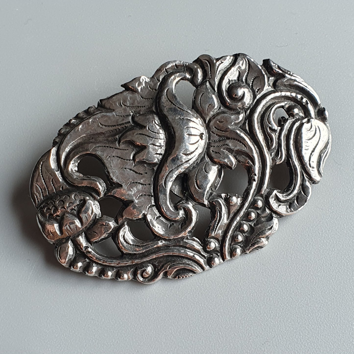 Ornate silver brooch with intricate floral and scrollwork designs.