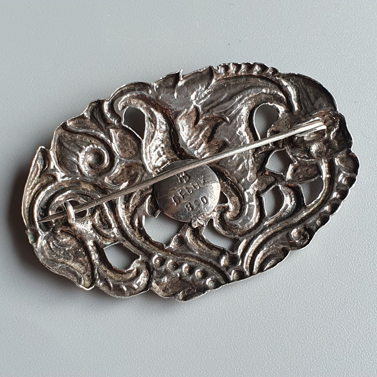 Ornate silver brooch with intricate swirling designs and a central pin.