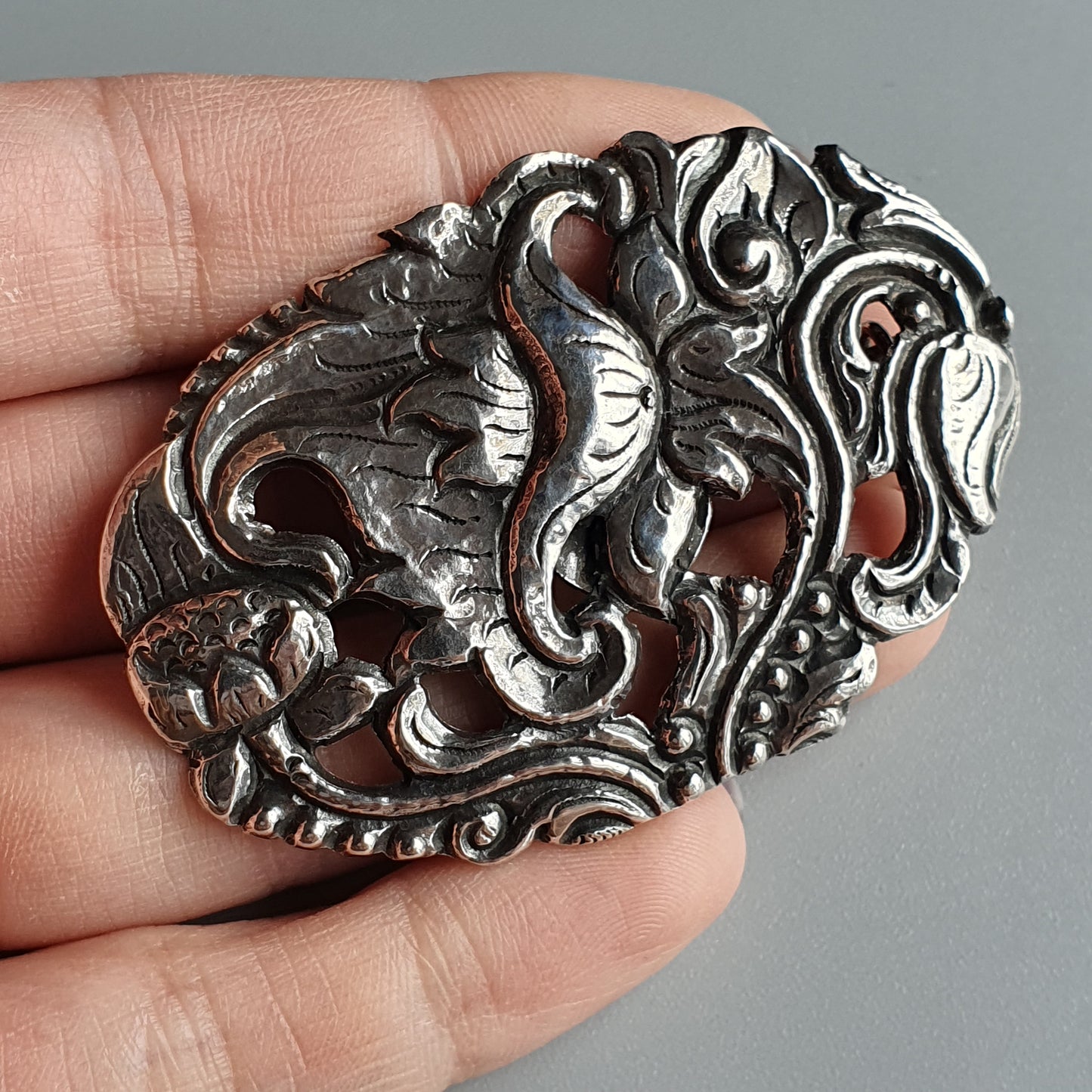 Ornate silver brooch or pendant with intricate floral and swirling designs.